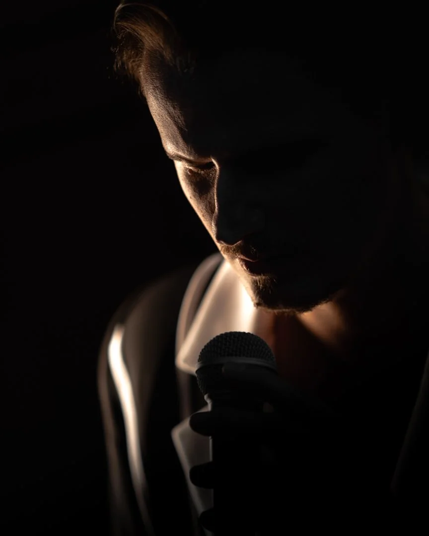 A person holding a microphone in a dark setting with outline lighting on their face, focusing on the side profile.