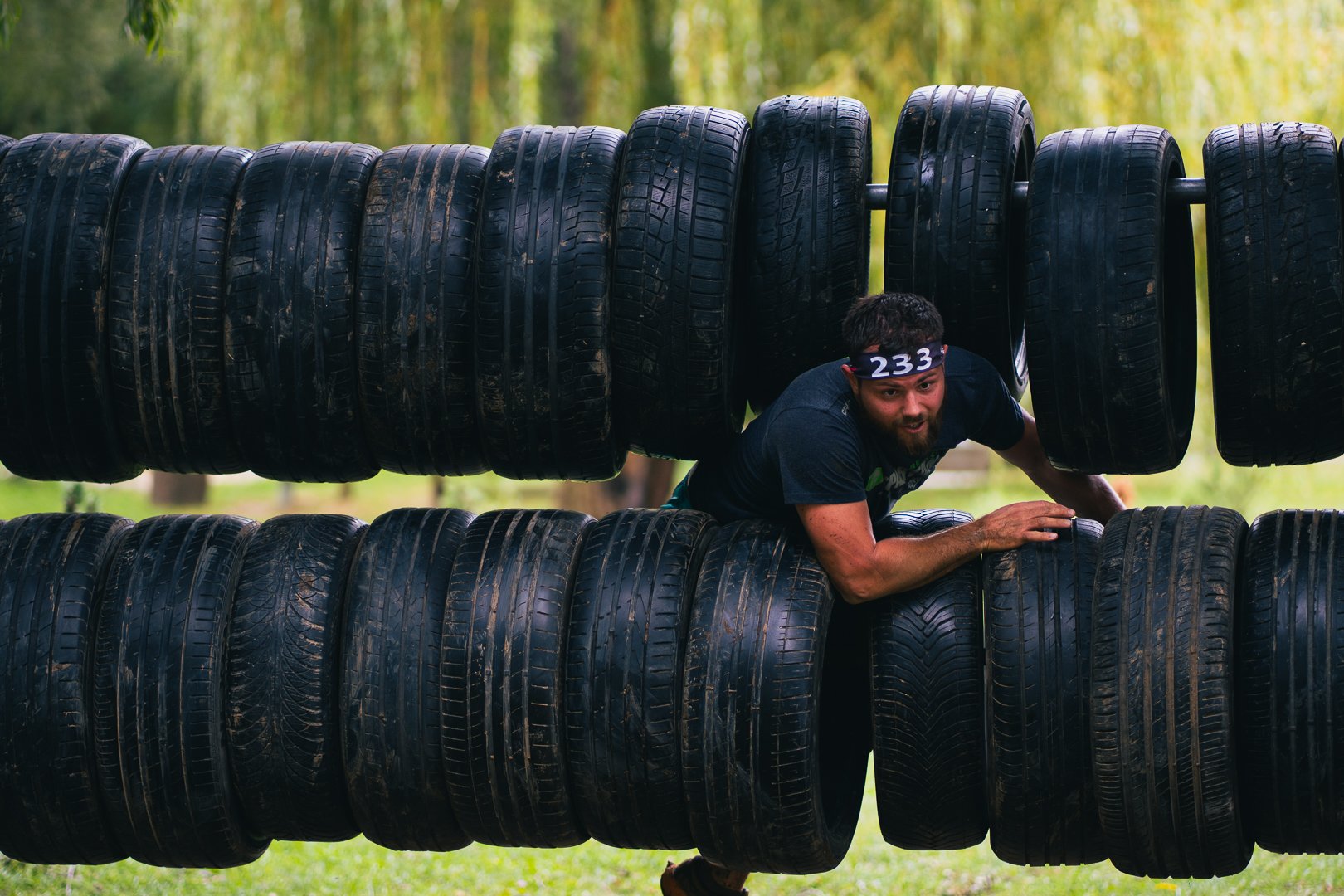 A man participating in an obstacle course challenge, crawling through a tunnel made of stacked tires outdoors.