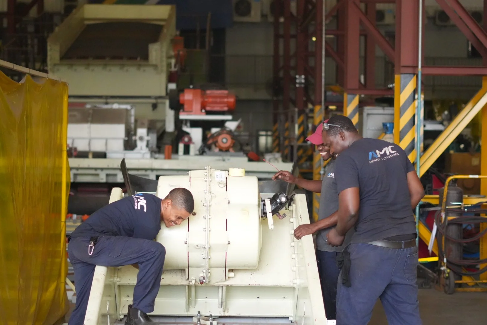 Three men working and laughing around industrial equipment in a factory or workshop setting.