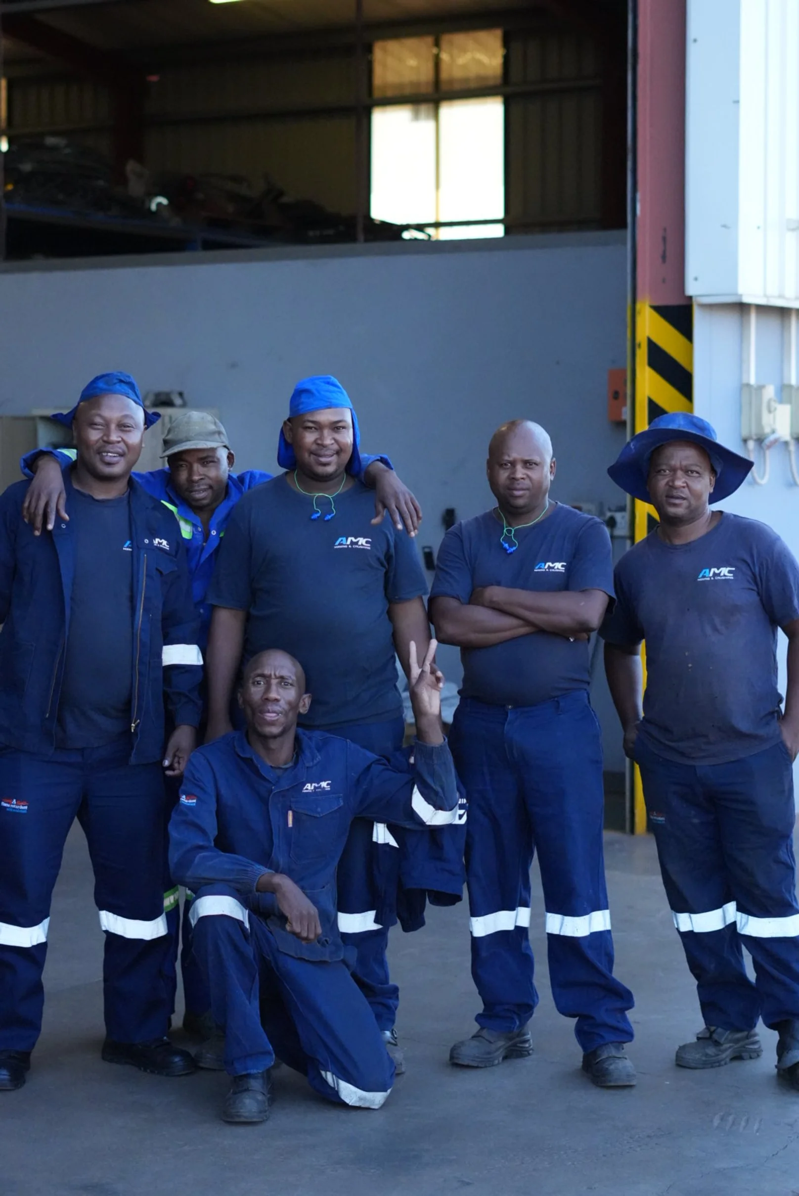 Group of six workers in blue uniforms posing inside an industrial facility.