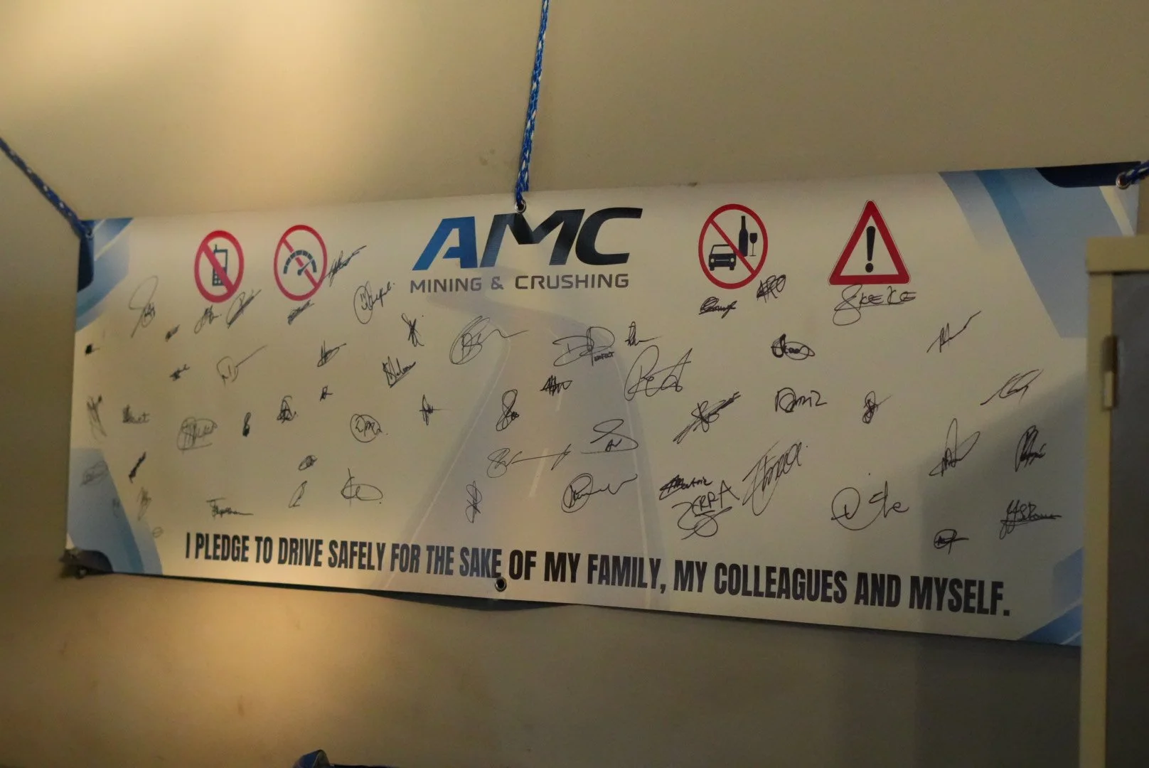 Sign with 'AMC Mining & Crushing' logo, safety warnings, and signatures, including a pledge to drive safely for the sake of family, colleagues, and oneself.