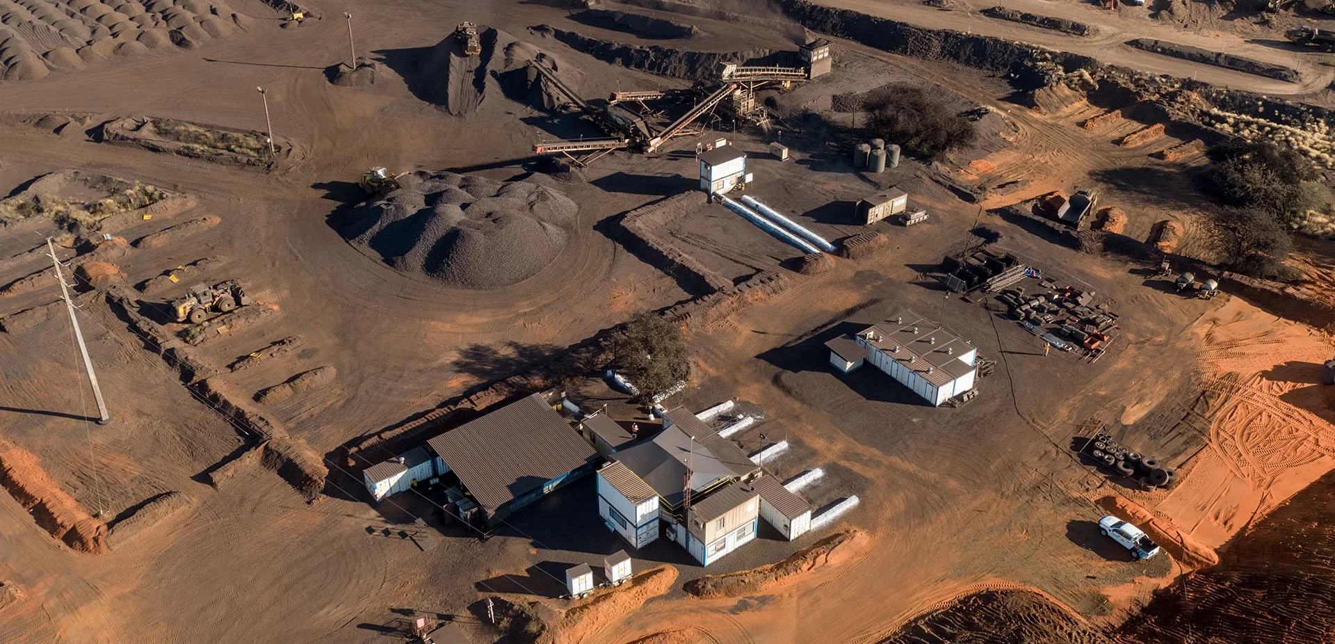 An aerial view of a construction or mining site with piles of dirt, machinery, equipment, and temporary buildings.