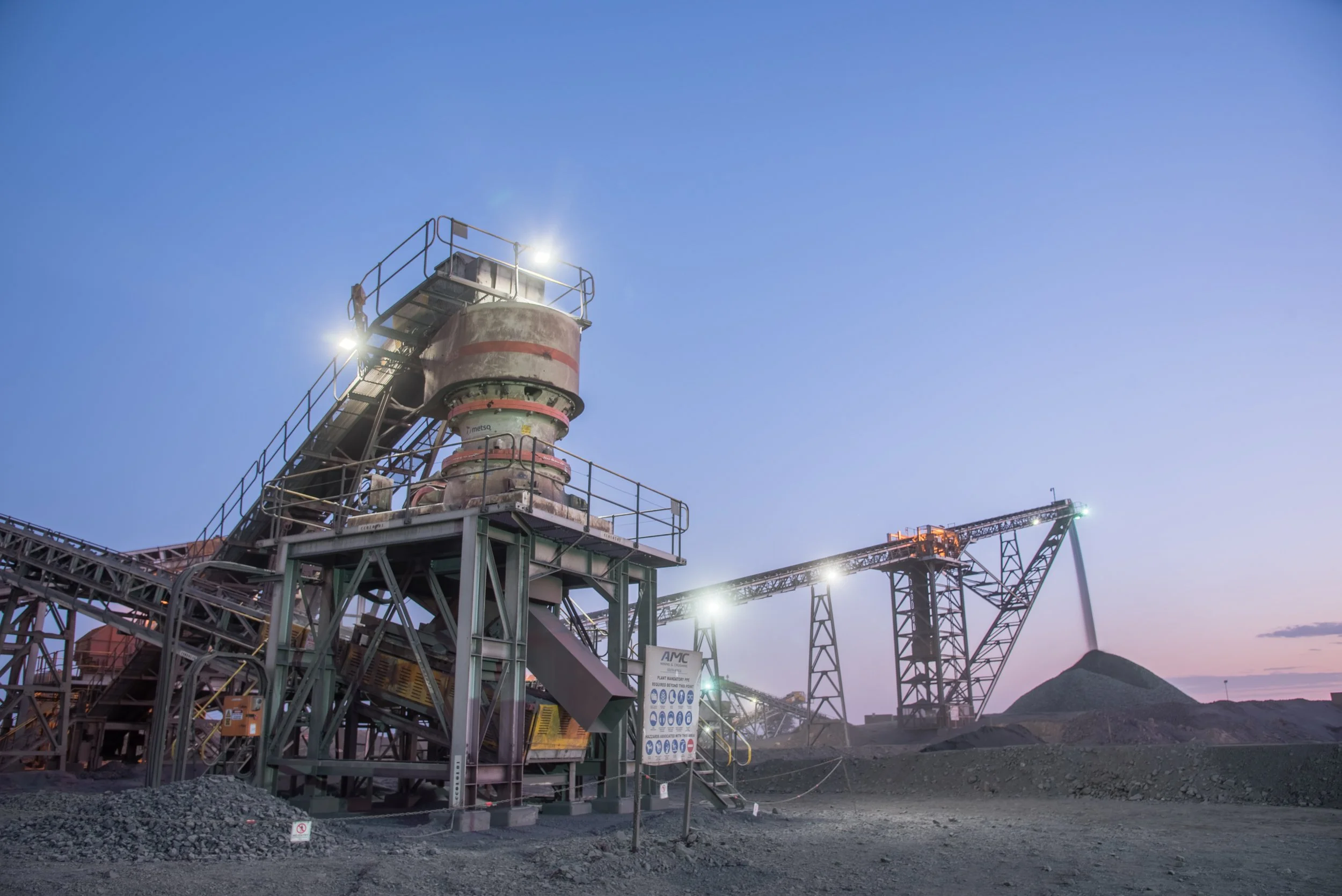 Industrial mining equipment with conveyor belts and a large hill of extracted material under a twilight sky.
