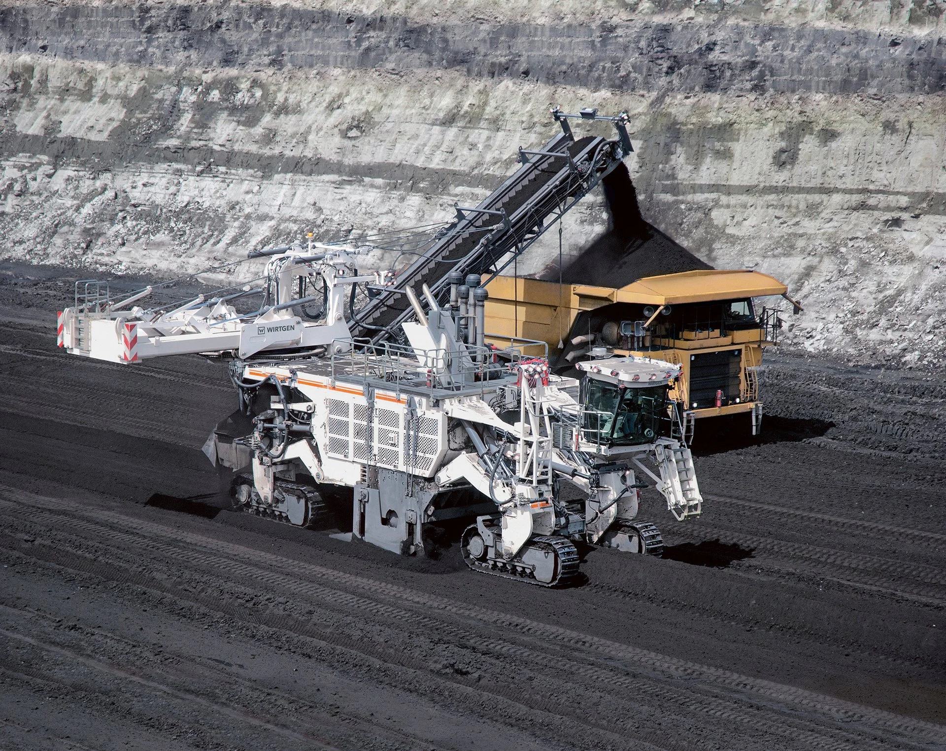 Large industrial machine with tracks, unloading black coal onto a pile at a mining site.