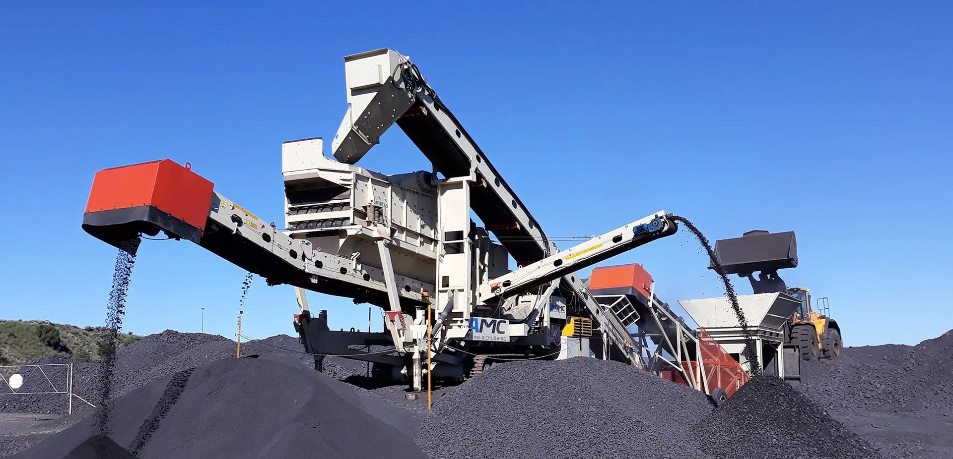 Mining machine processing black coal piles under clear blue sky