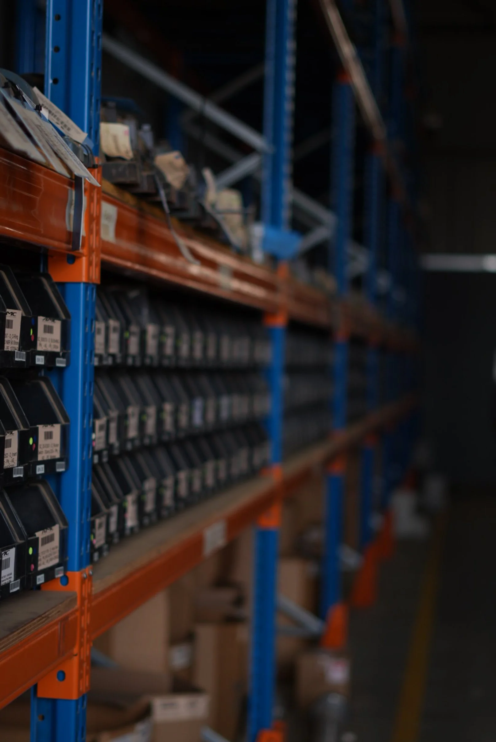 Industrial warehouse shelving with small containers and boxes, partially filled, with blurry background.