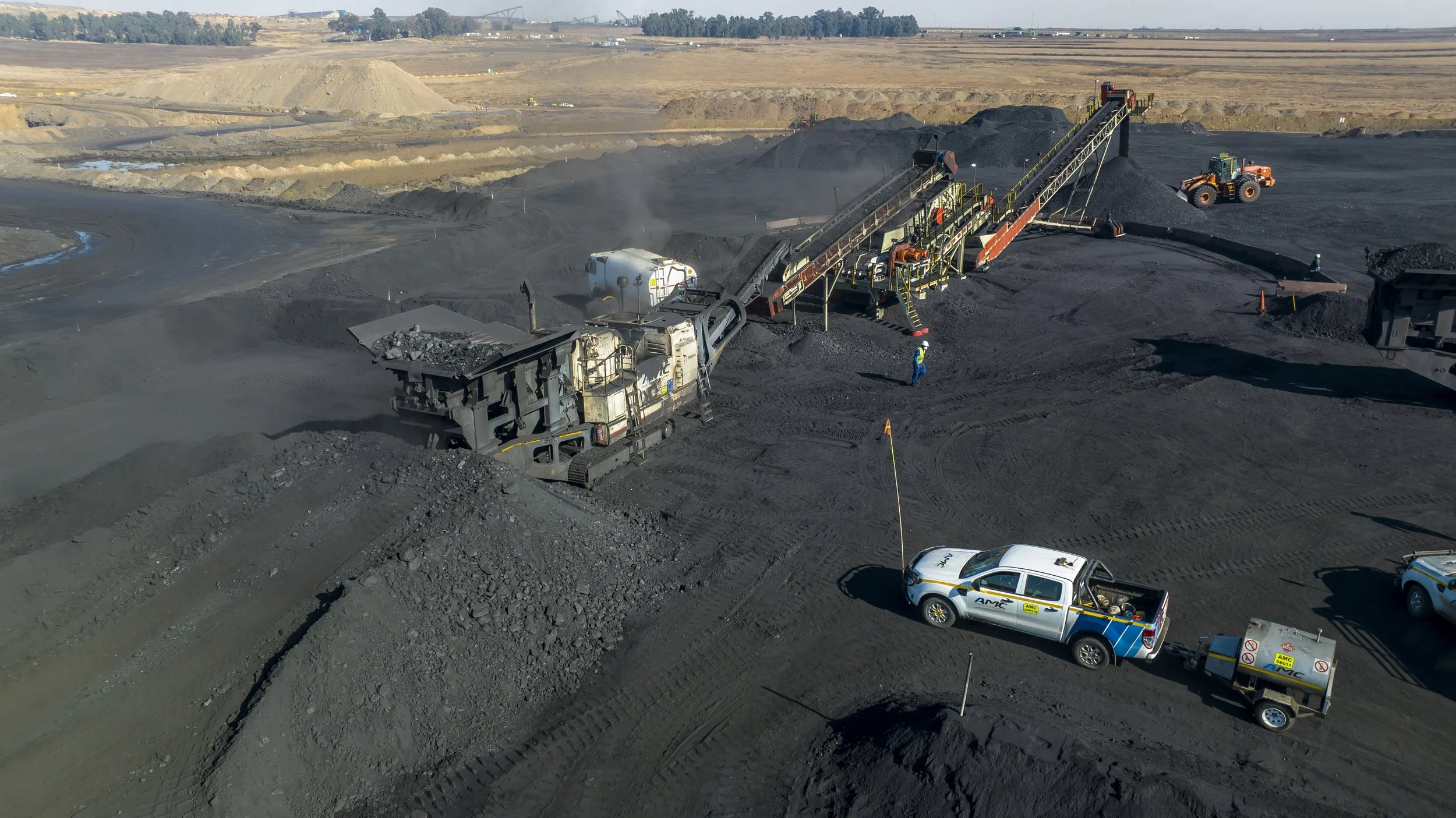 View of a mining operation with excavators and trucks; black coal being moved and processed, with trucks transporting coal and machinery working on the site.