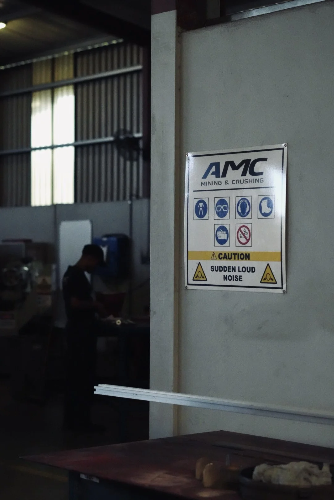 Sign for AMC Mining & Crushing with safety instructions and caution for sudden loud noise inside an industrial or mining facility.