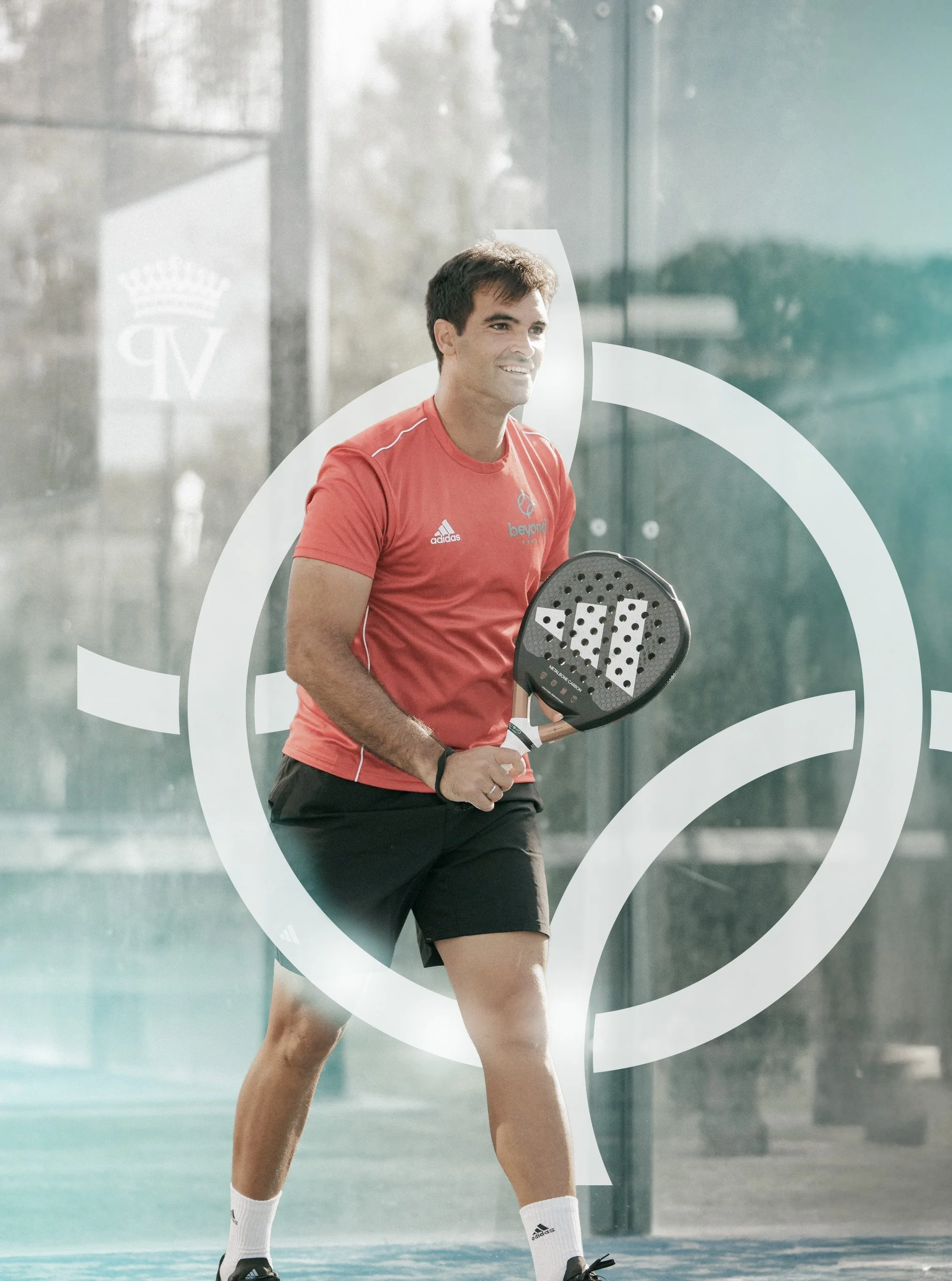 A man is playing paddle tennis on an indoor court, holding a paddle and smiling.