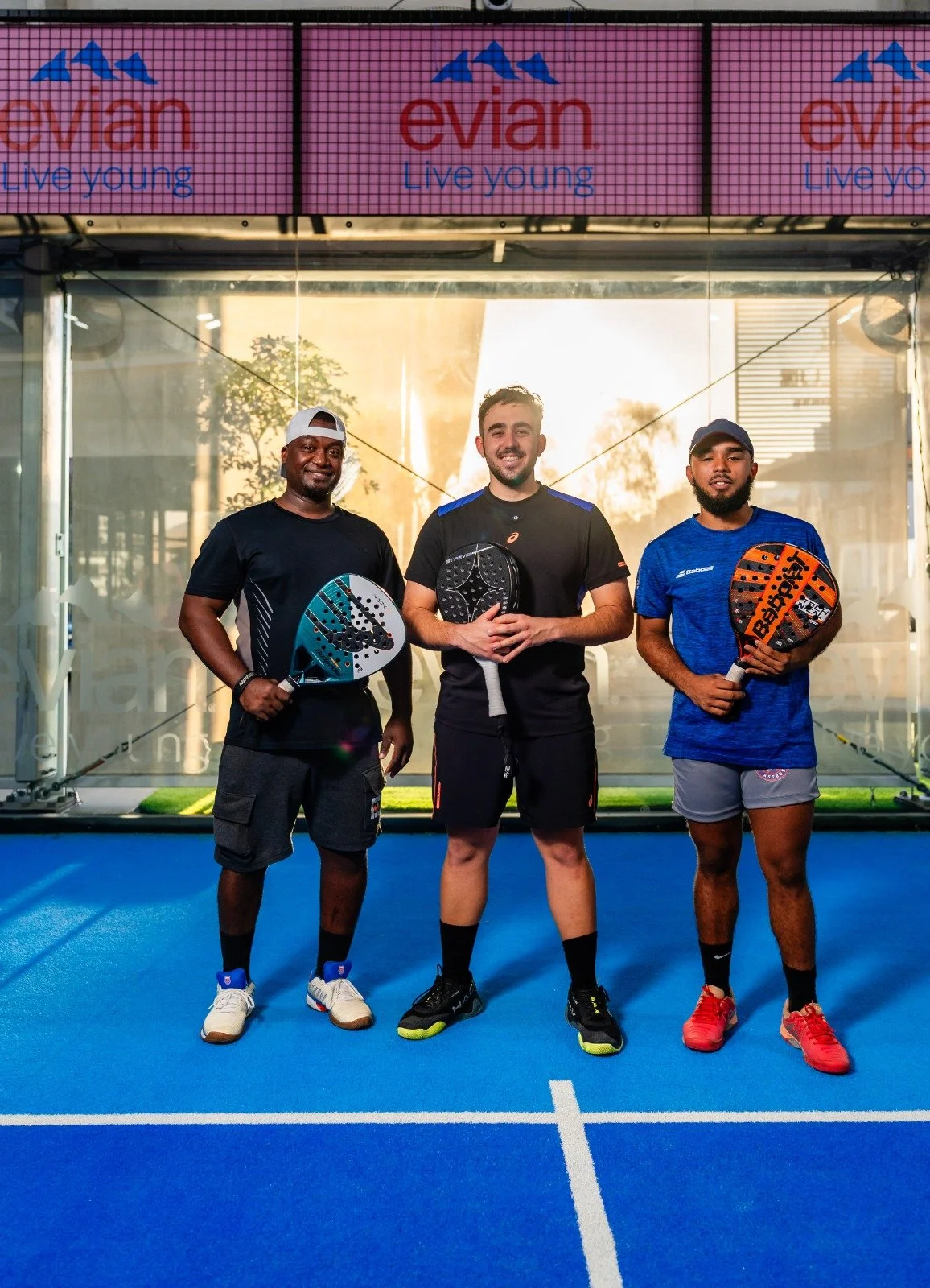 A man playing paddle tennis on an indoor court, dressed in blue sports attire, hitting a yellow ball with a paddle.