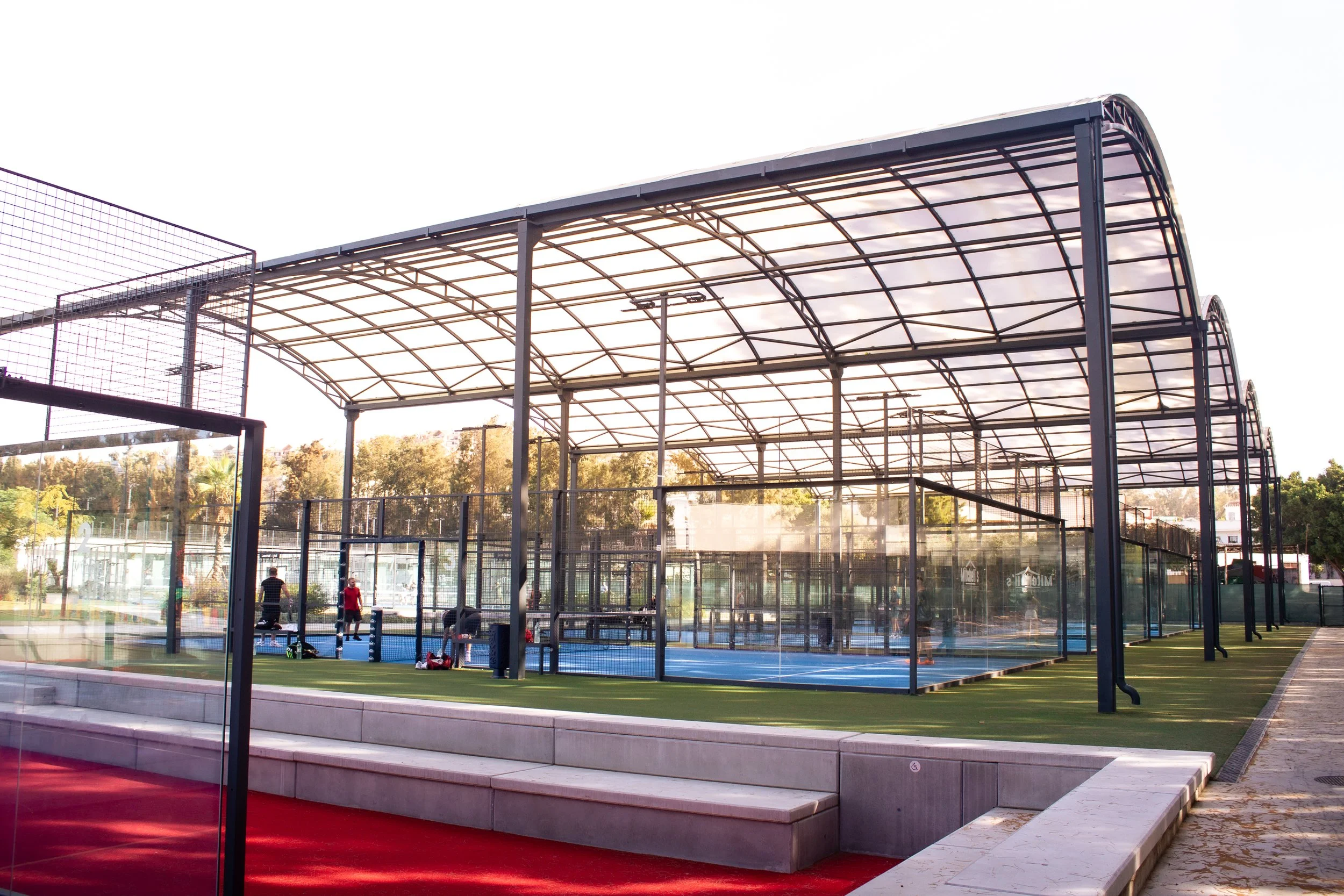 An outdoor sports courts with a covered roof and fencing, with children playing.