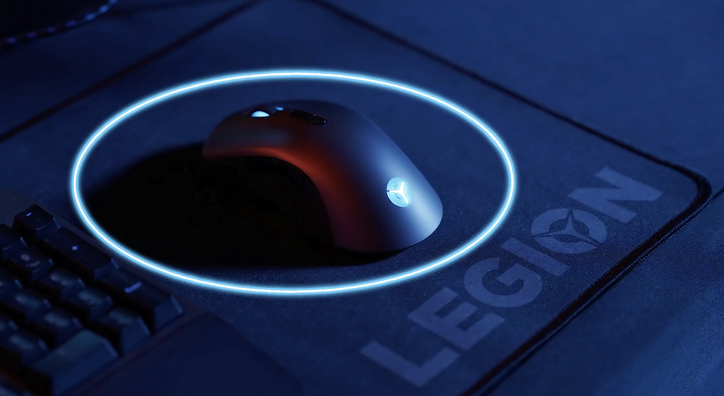 A gaming mouse with the logo, illuminated in blue, is placed on a mouse pad with the logo and text, surrounded by a glowing blue circle.