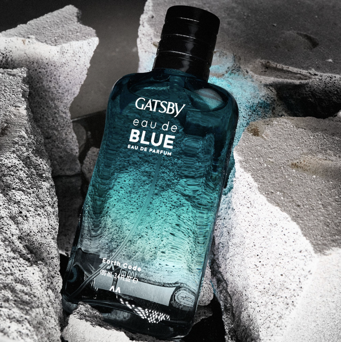 A blue bottle of Gatsby Eau de Parfum on rocks and sand.