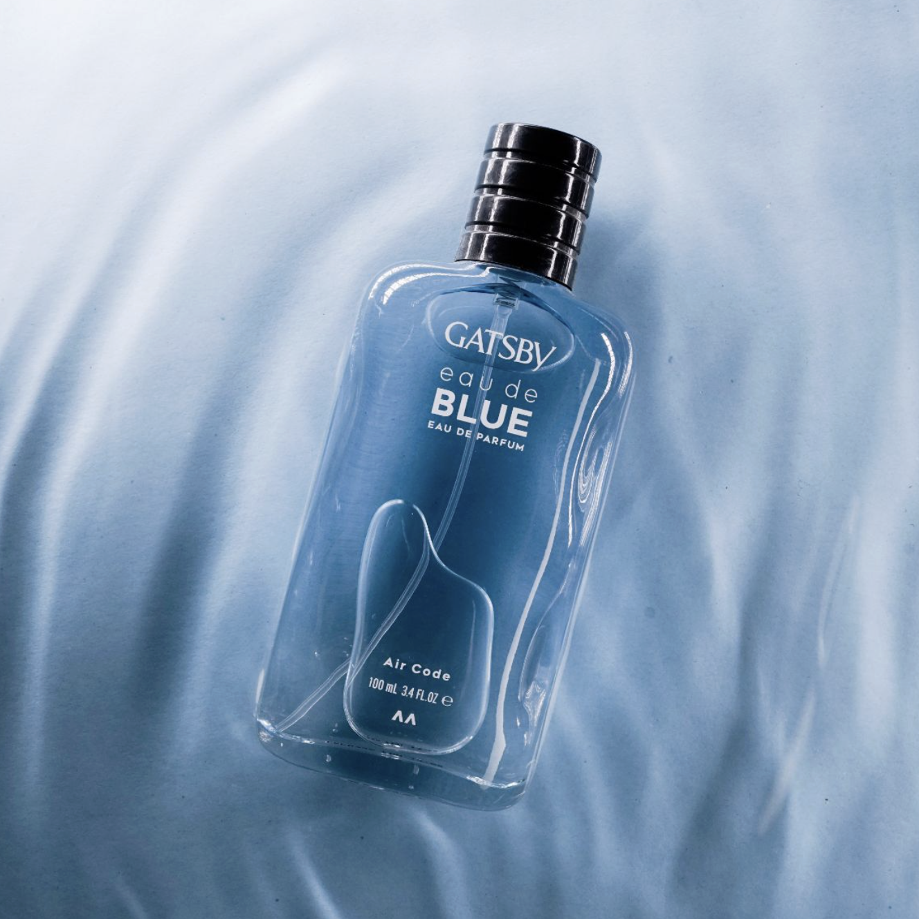 A bottle of Gatsby Eau de Blue perfume lying on a light blue, silky fabric surface.