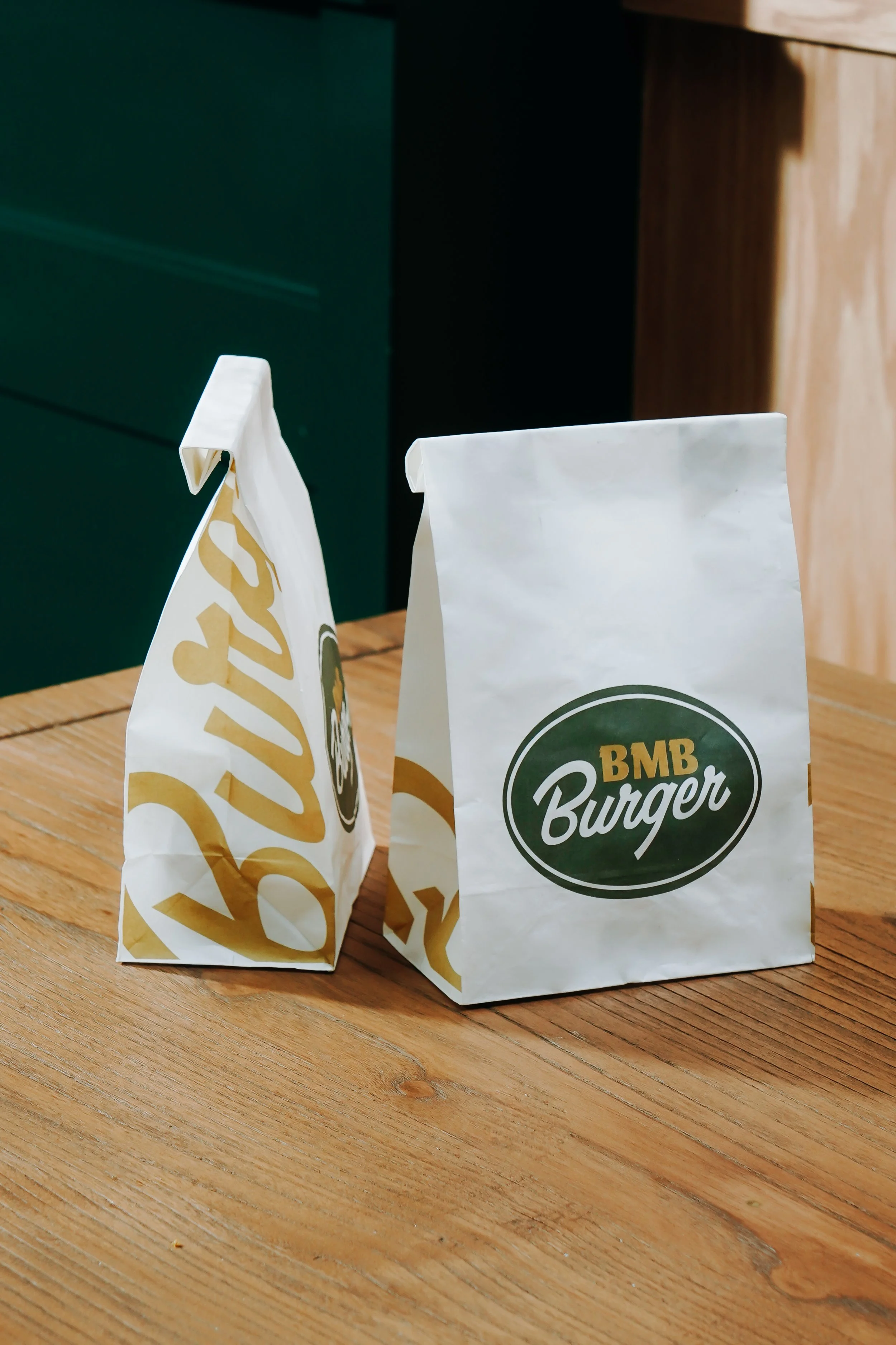 Two white paper bags with green and gold logos, placed on a wooden table.