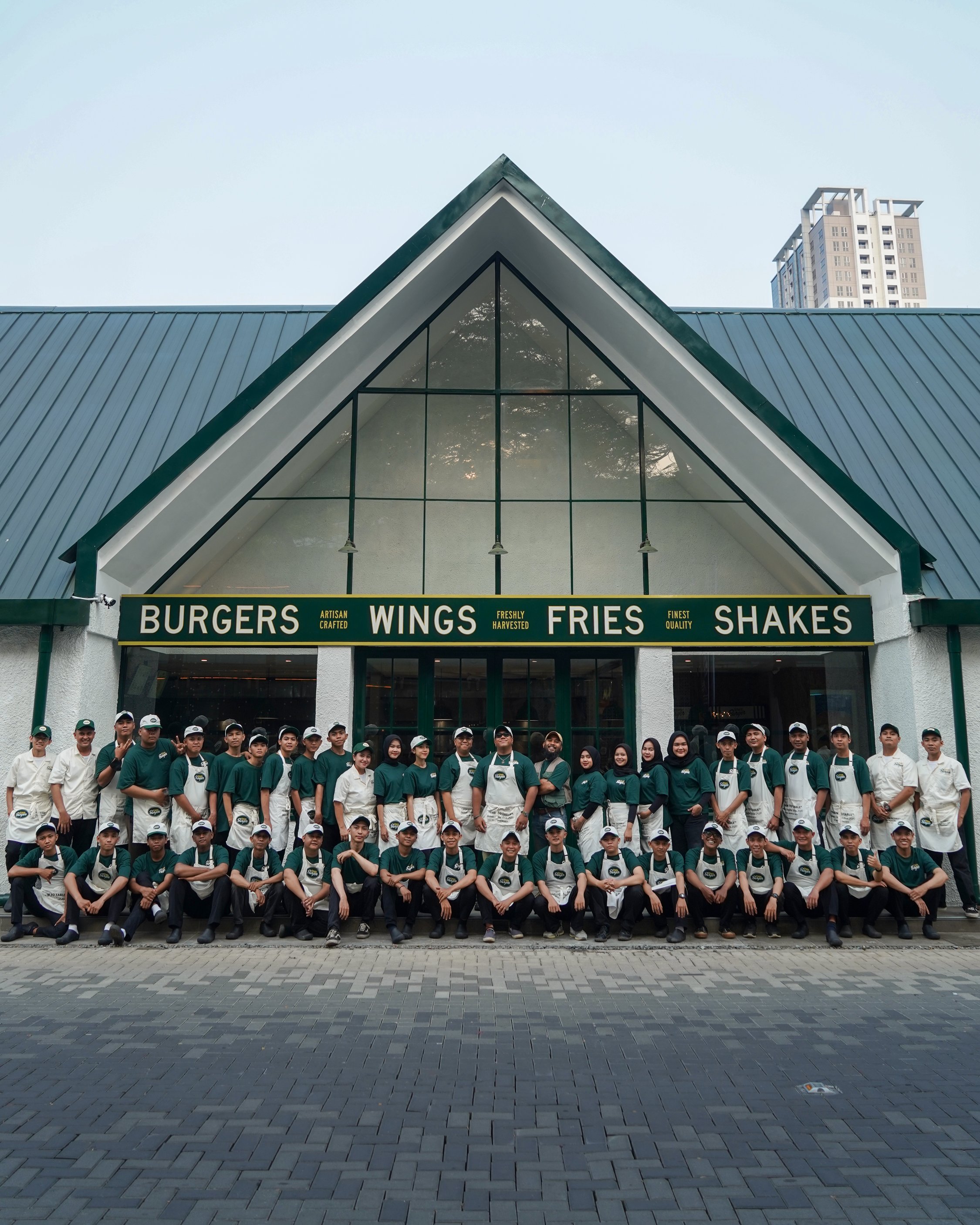 Group of restaurant employees in uniform posing in front of a restaurant with a sign that says Burgers, Wings, Fries, Shakes.