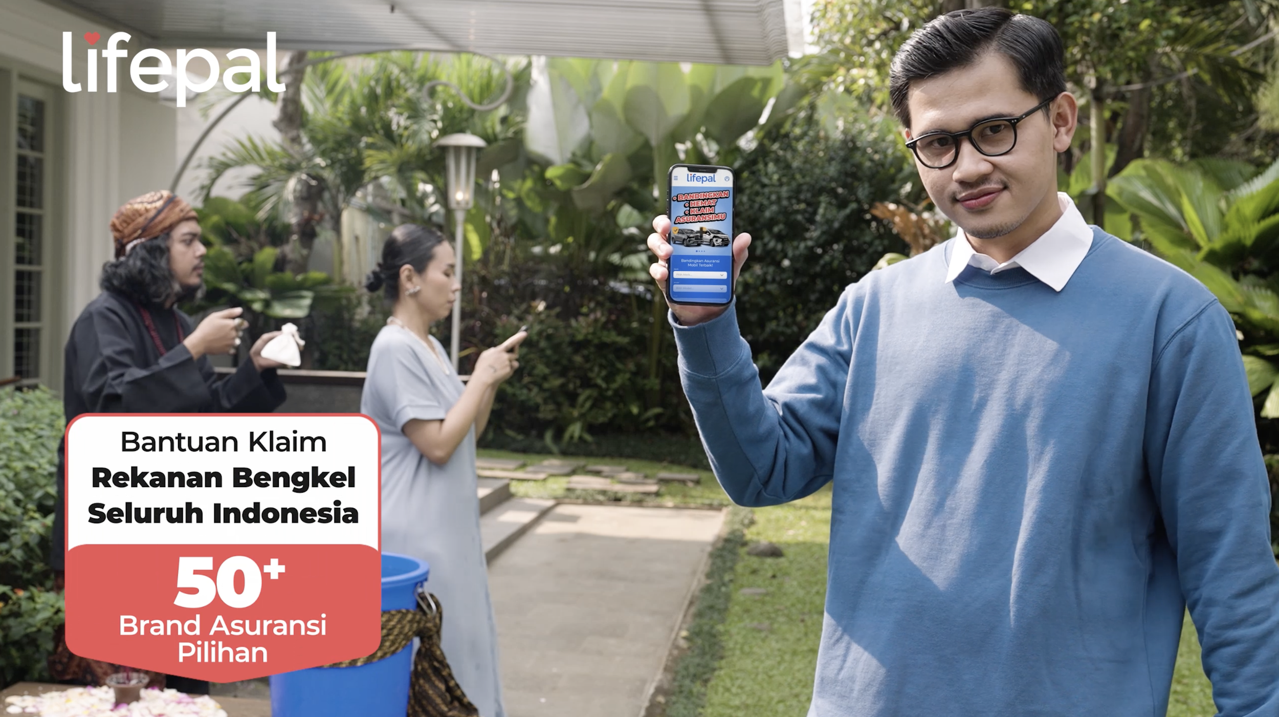 A man in glasses and a blue sweater holding a smartphone displaying the Lifepal app, outdoors with green plants, and two women in the background looking at their phones.