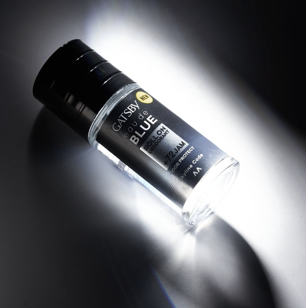 A bottle of Gatsby Eau de Blue roll-on deodorant with black cap and label, positioned on a dark and light gradient background.