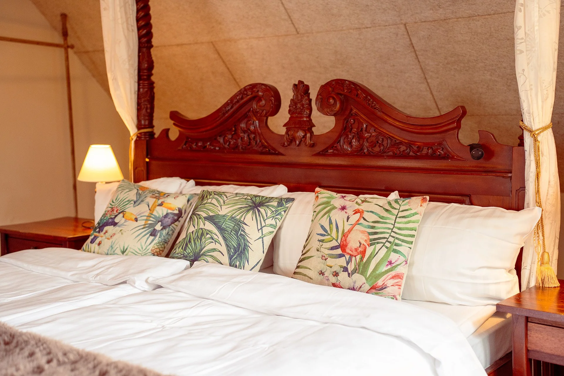 Udskåret sengegavl, tropiske puder, hvidt sengetøj