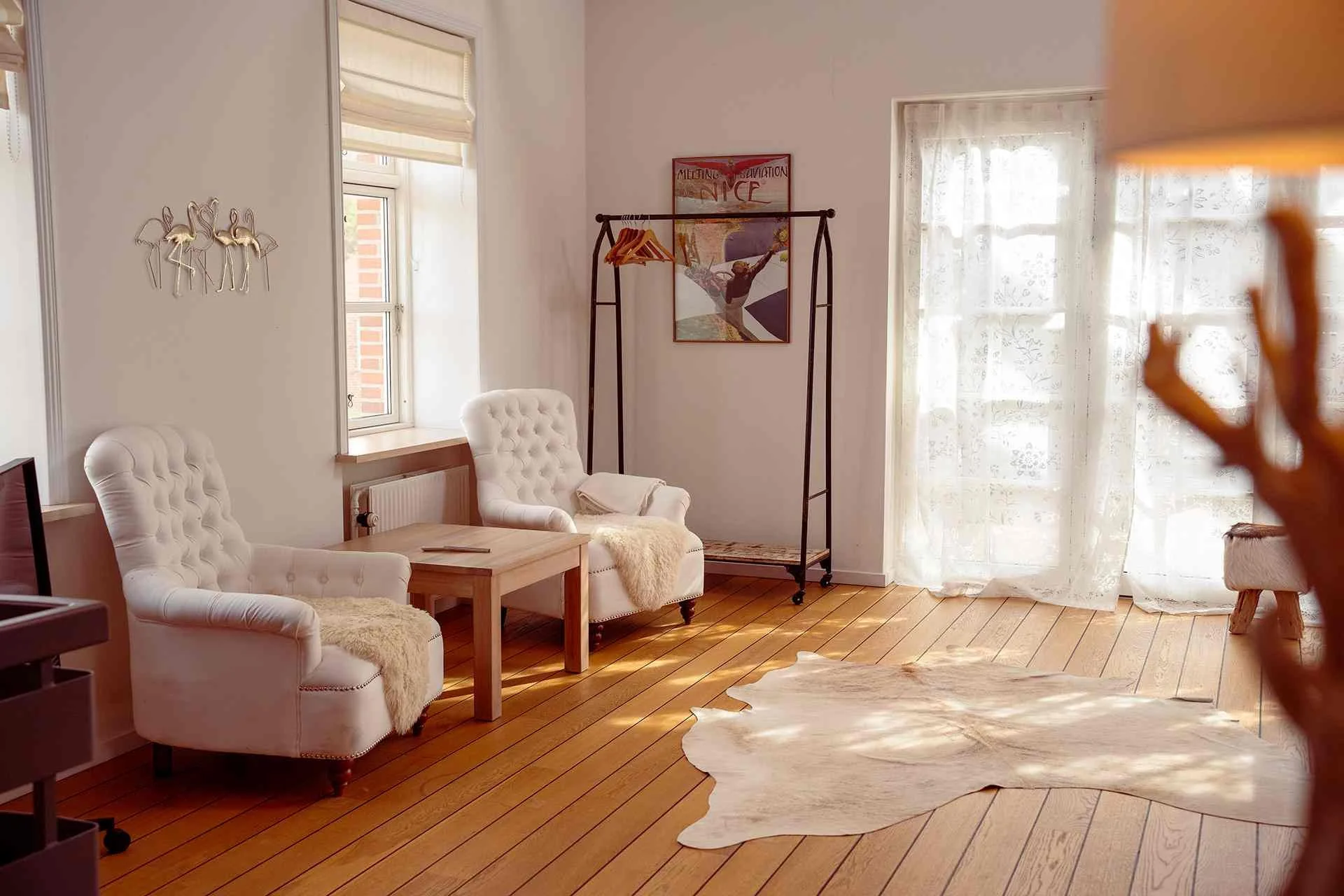 Lys loungestue, hvide capitonné lænestole, koekskin tæppe, vintage rejseplakater