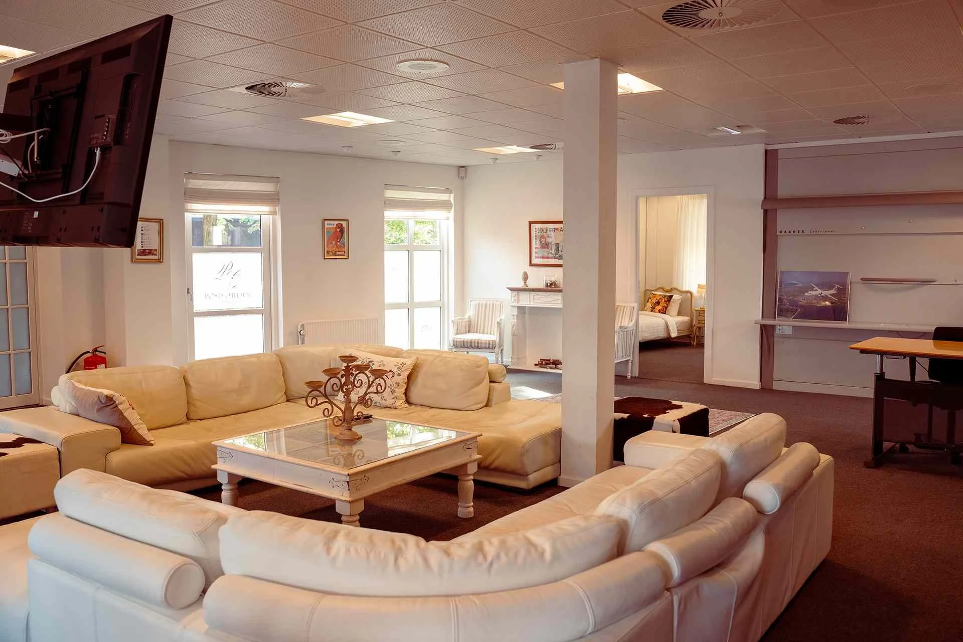 Rummelig stue overblik, hvid sofa, glassbord, verdenskort kunst, åbent køkken