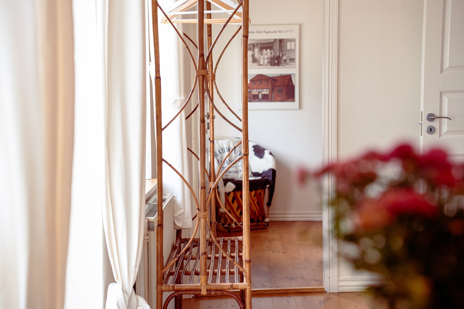 Rotting møbelstativ, lyse gardiner, røde blomster, entre