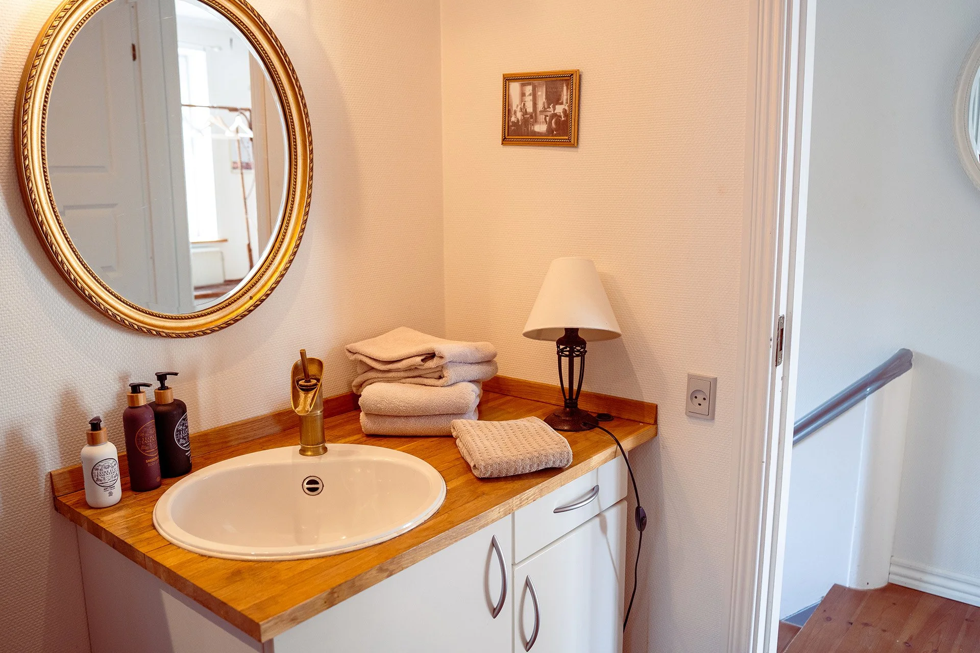 Håndvask, guldrundt spejl, træbordplade, håndklæder