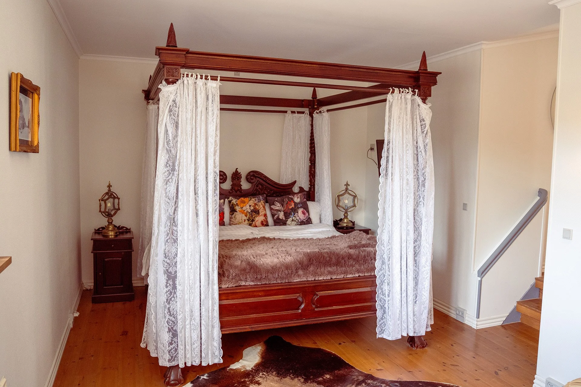 Himmelseng med blondegardiner, blomstrede puder, koekskin tæppe