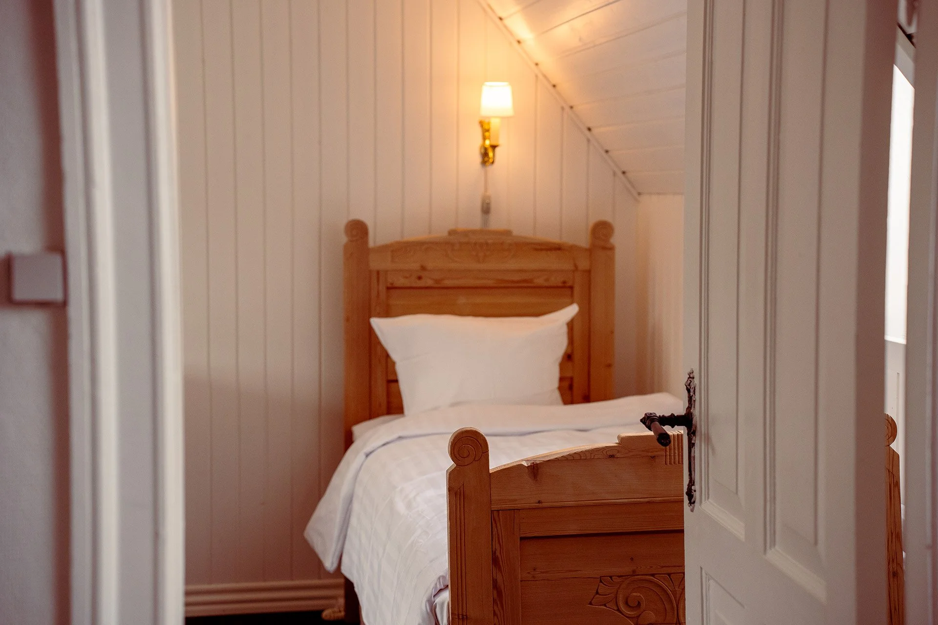 Træseng, hvidt sengetøj, væglampe, hvid dør