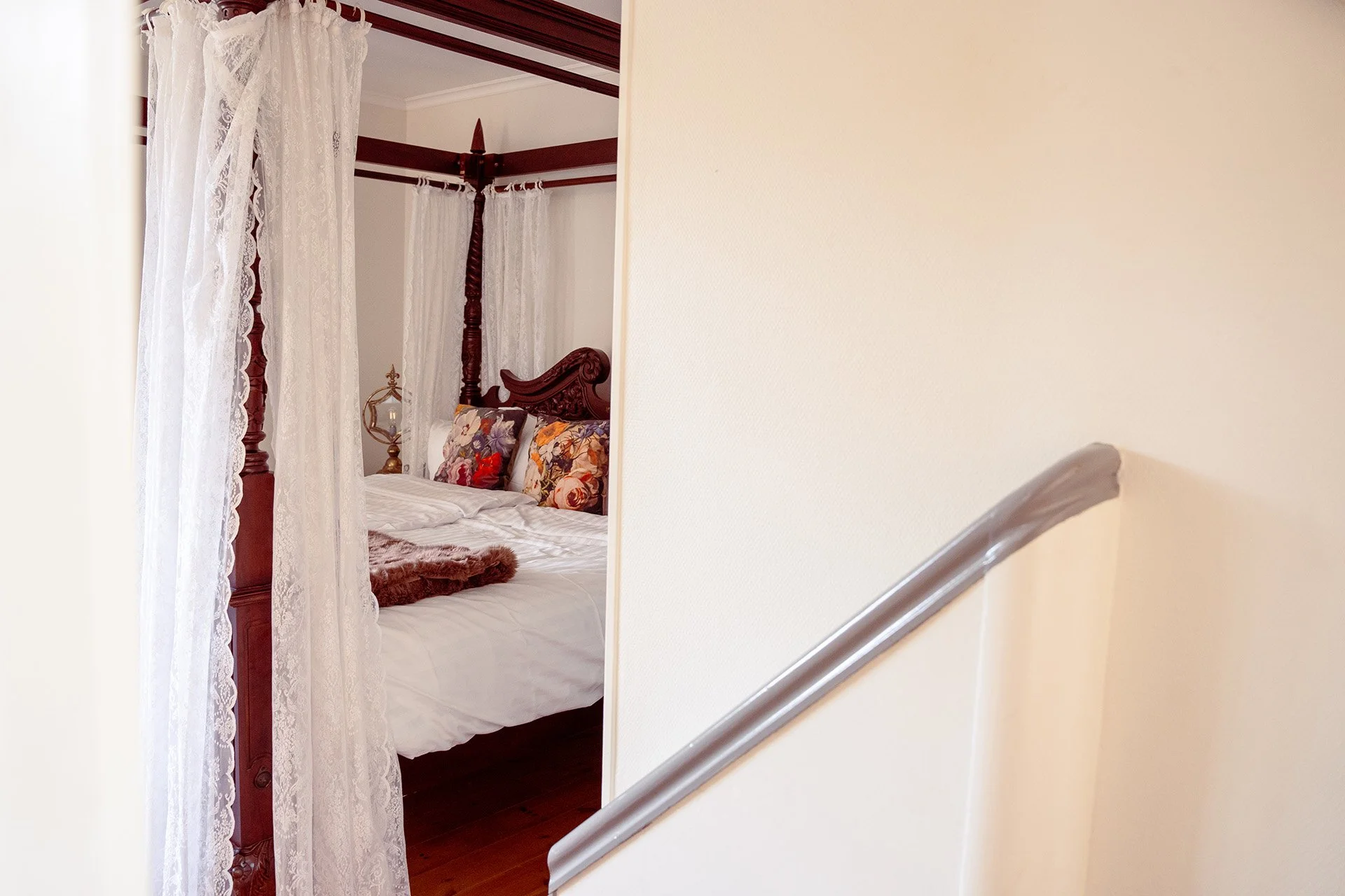 Himmelseng med blondegardiner, blomstrede puder, trappe