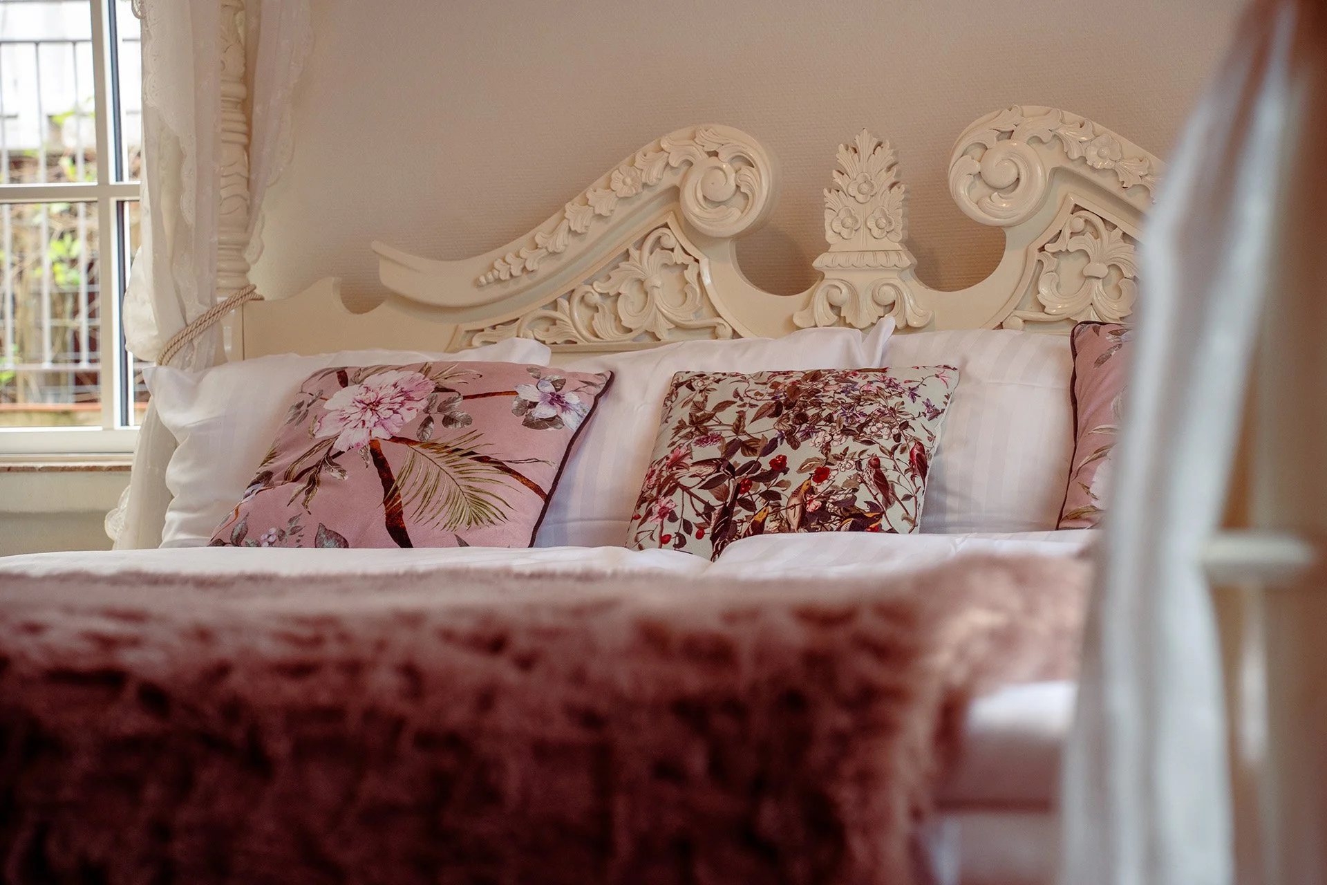 Udskåret hvid sengegavl, rosa puder, sengelampe, baldakin