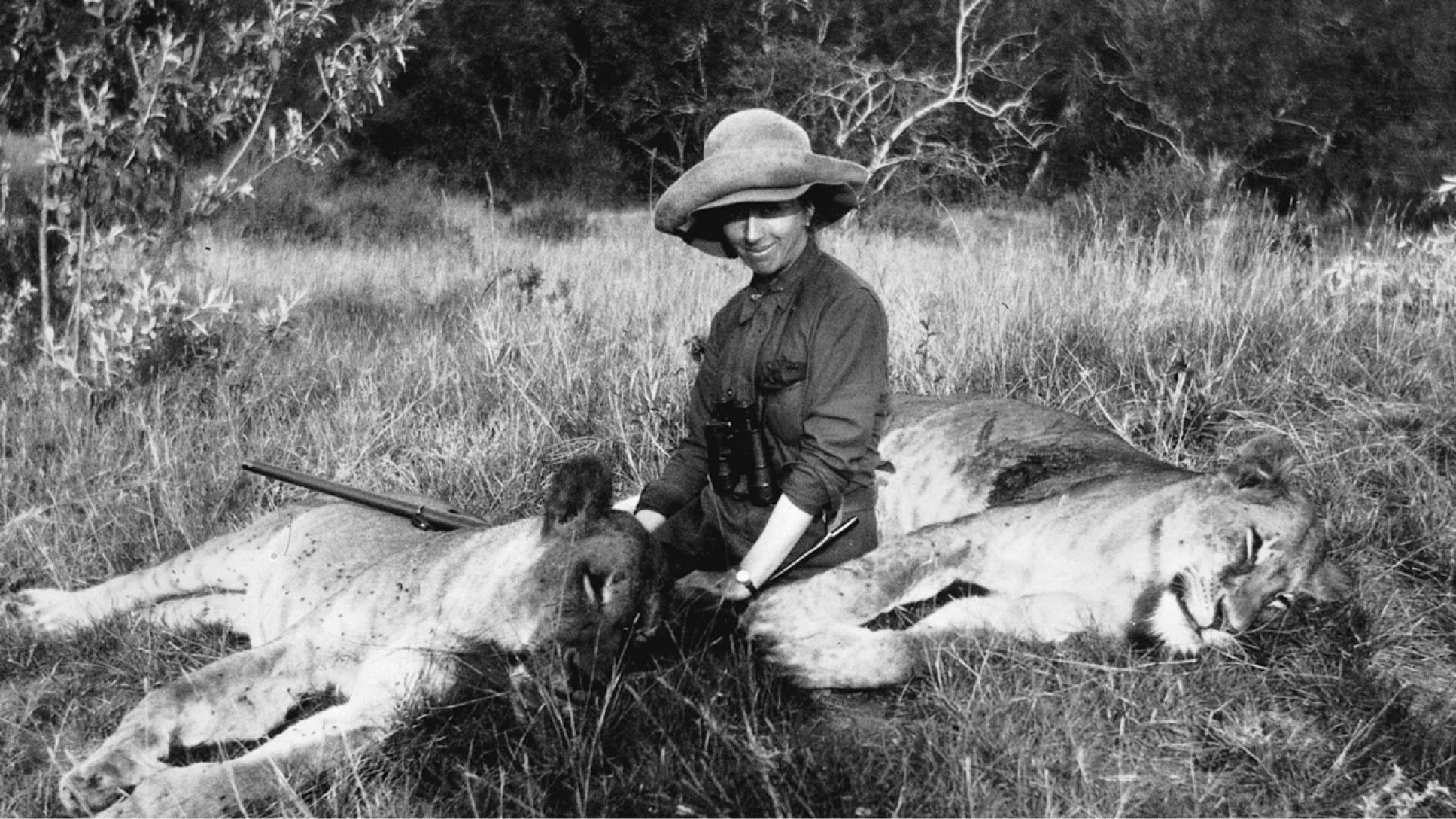 Sort-hvid billede af en kvinde med hat, der sidder på græs med to døde geparder, mens hun holder en rifle.