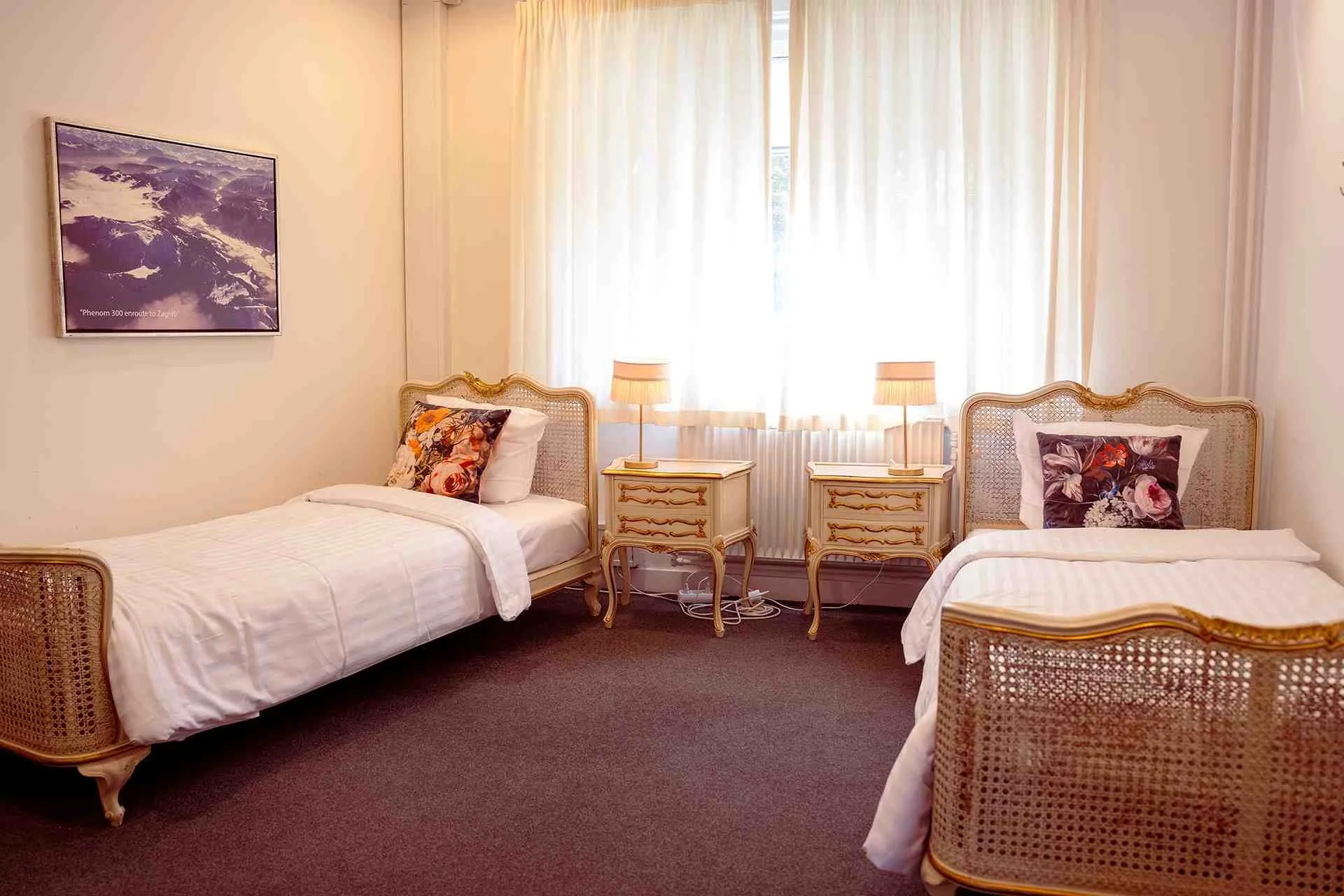 Lyst tvillingeværelse, forgyldte senge, blomstrede puder, luftfoto kunst