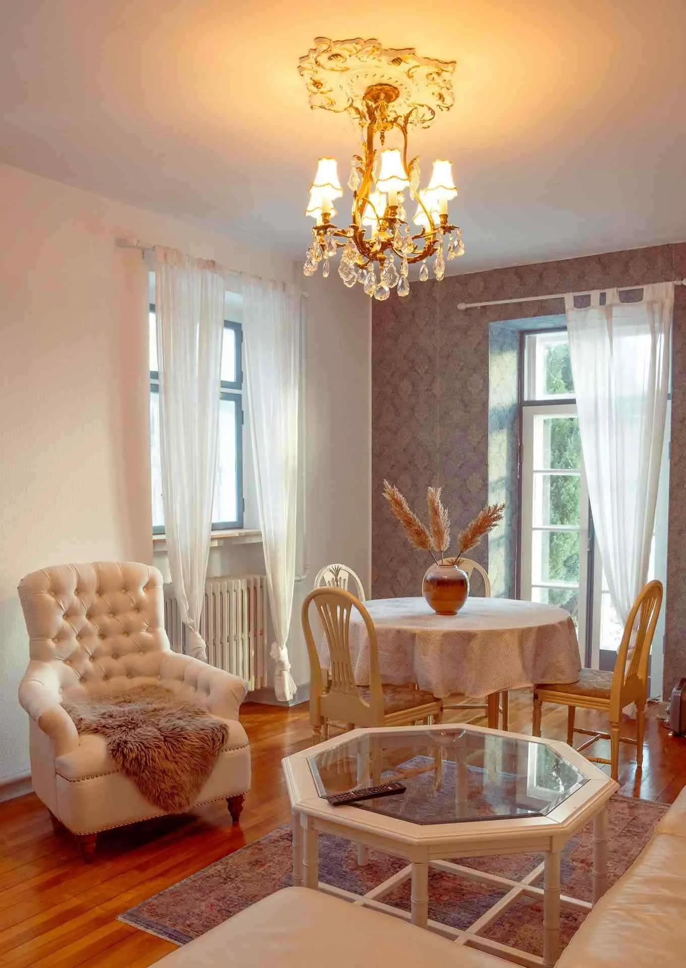 Guldkrone lysekrone, hvid lænestol, damask tapet, sofabord