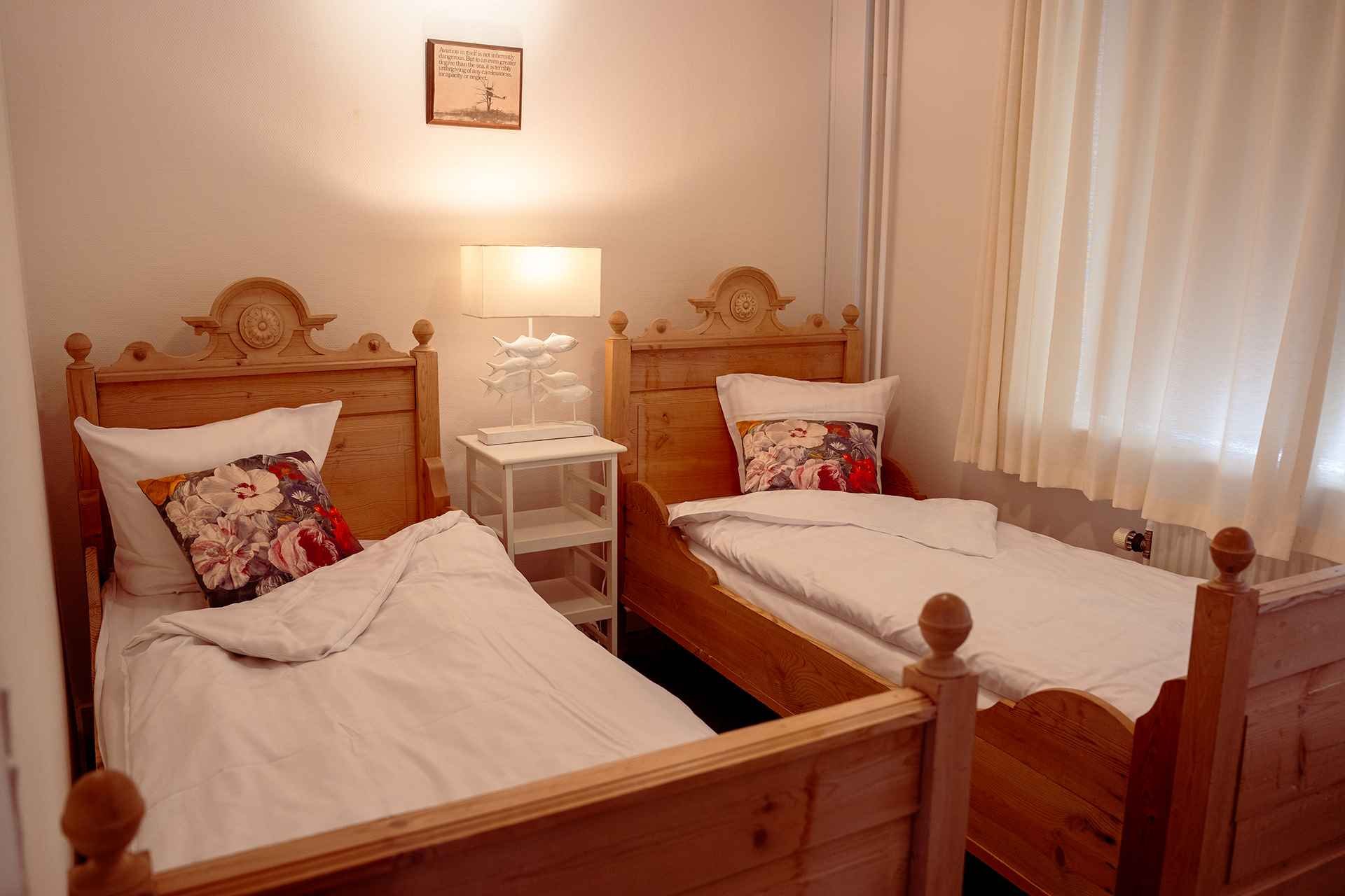 Hyggelig tvillingestue, udskårne træsenge, blomstrede puder, varmt aftenlys