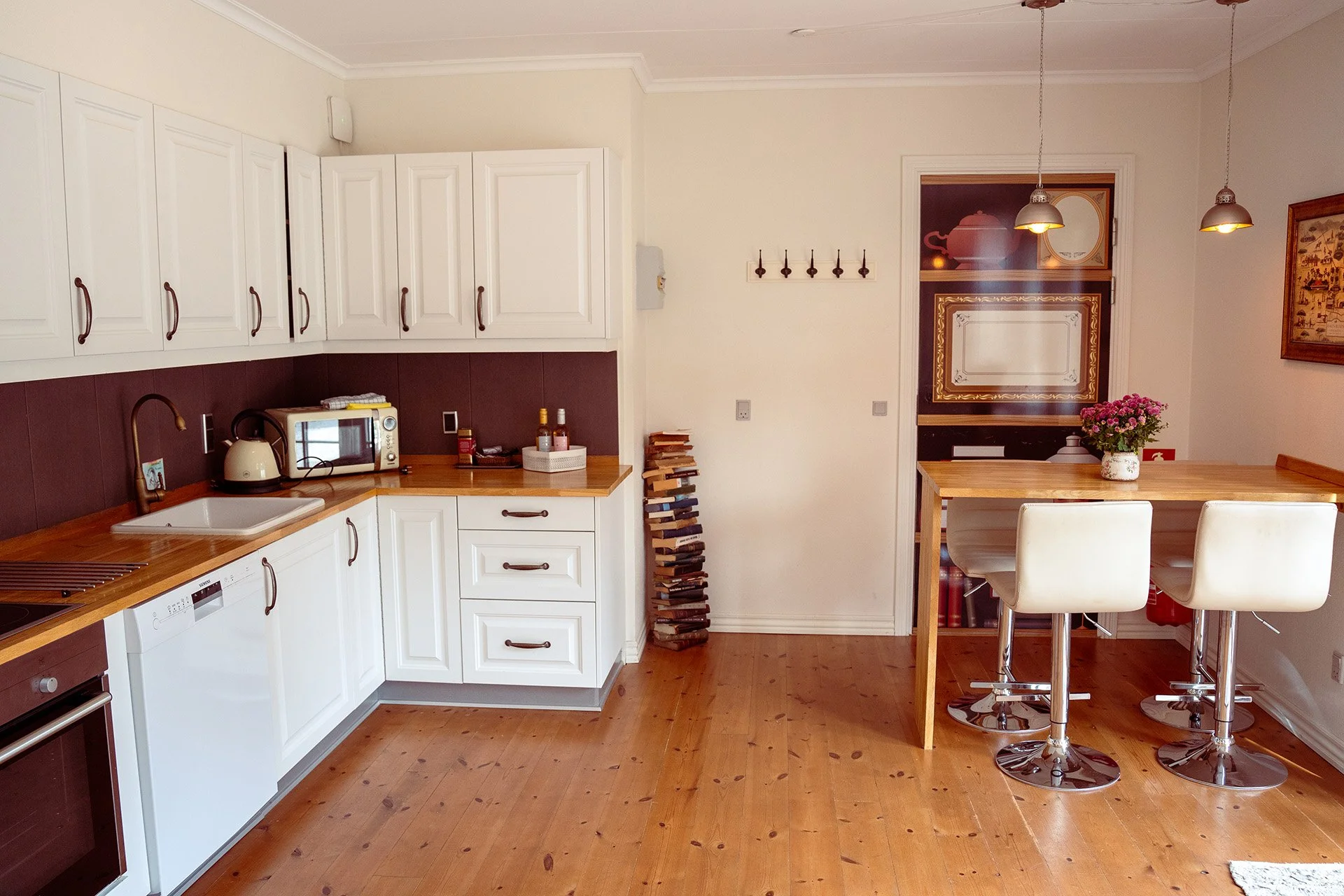 Hvidt køkken, træbordplade, højbord med barstole, bogstabel