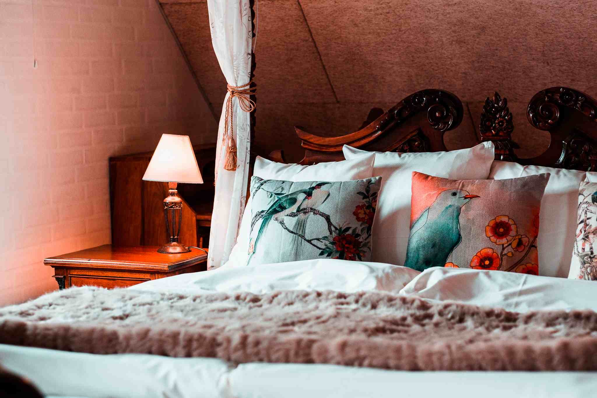 Udskåret sengegavl, blomstrede puder, sengelampe, aftenstemning