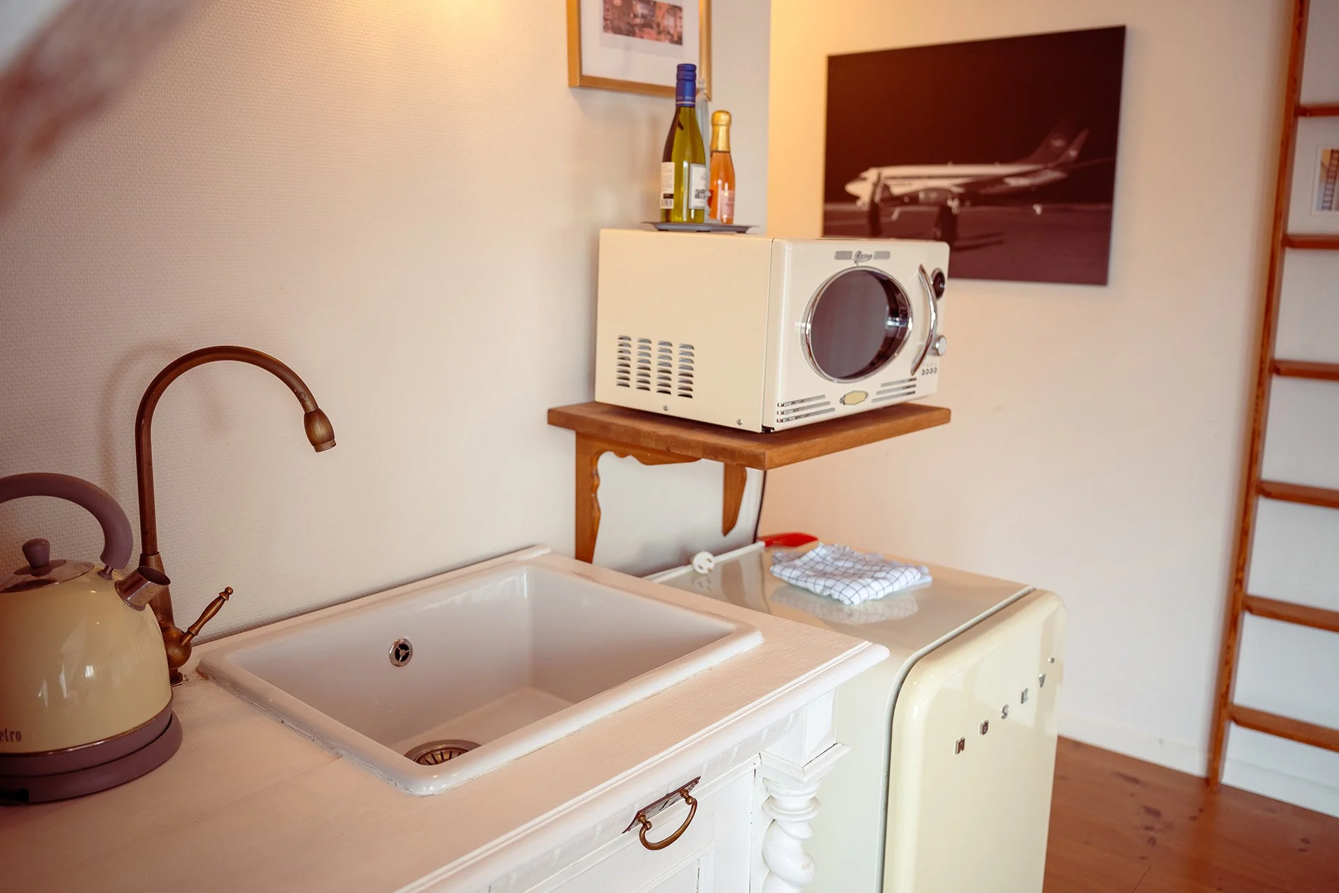 Vintage køkkenhjørne med vask, kedel, mikroovn og en koord på væggen.