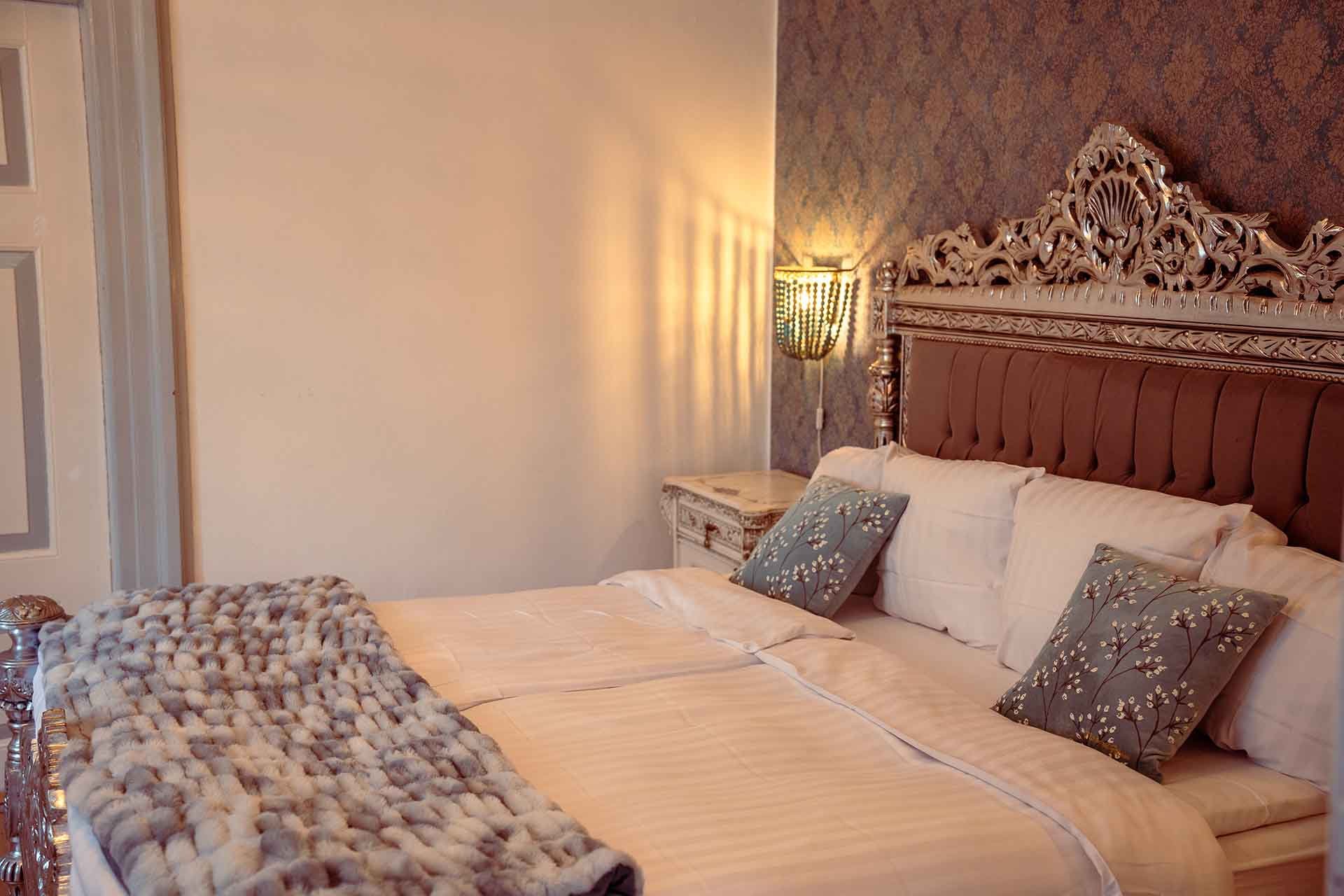 Sølv udskåret sengegavl, pelstæppe, grå puder, væglampe