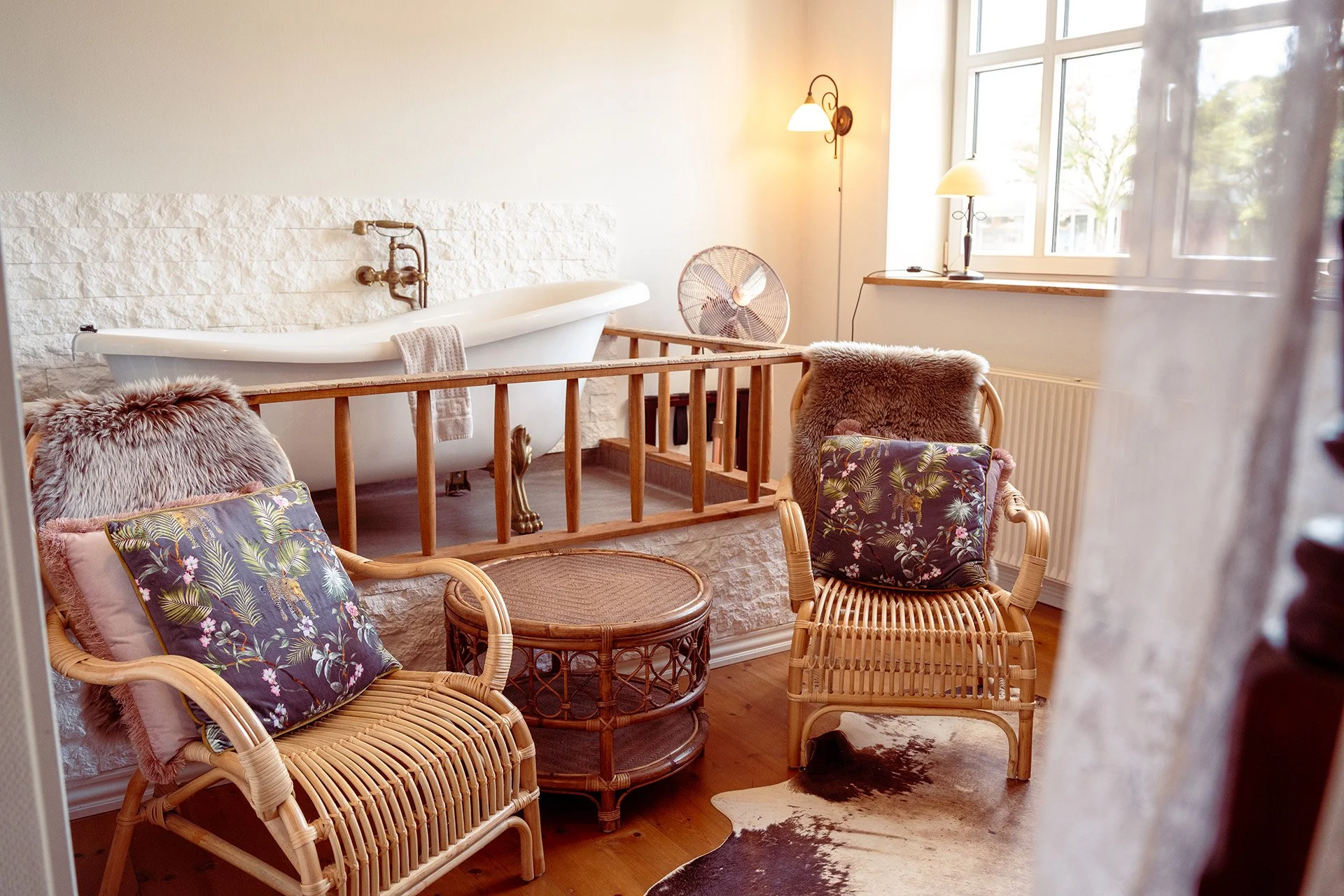Fritstående badekar, rotting lænestole, blomstrede puder, vindue