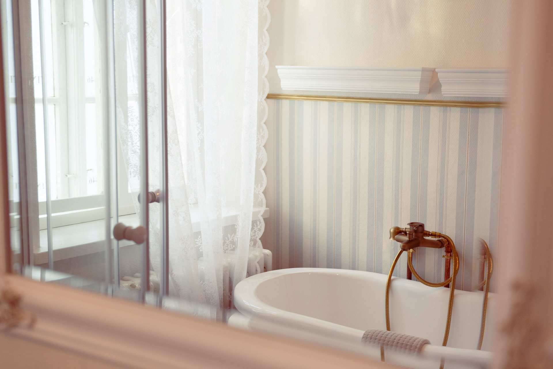 Badeværelse med fritstående badekar, messingarmatur, stripet tapet, bruser