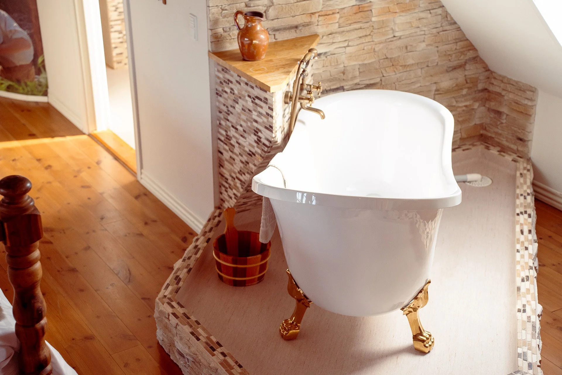 Fritstående badekar med guldfødder, mosaikfliser, stenmur