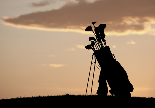 Silhuet af en golfkuffert og golfkøller mod en solnedgang