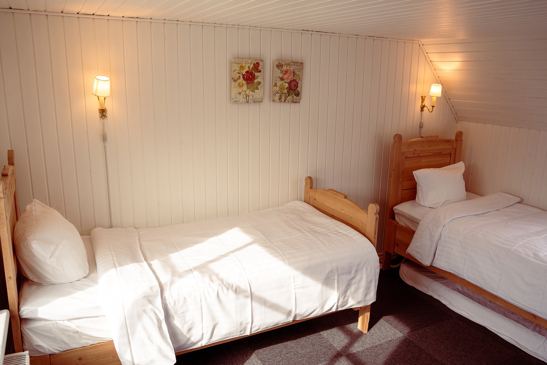 To enkeltsenge, træsengegavle, væglamper, lyst værelse