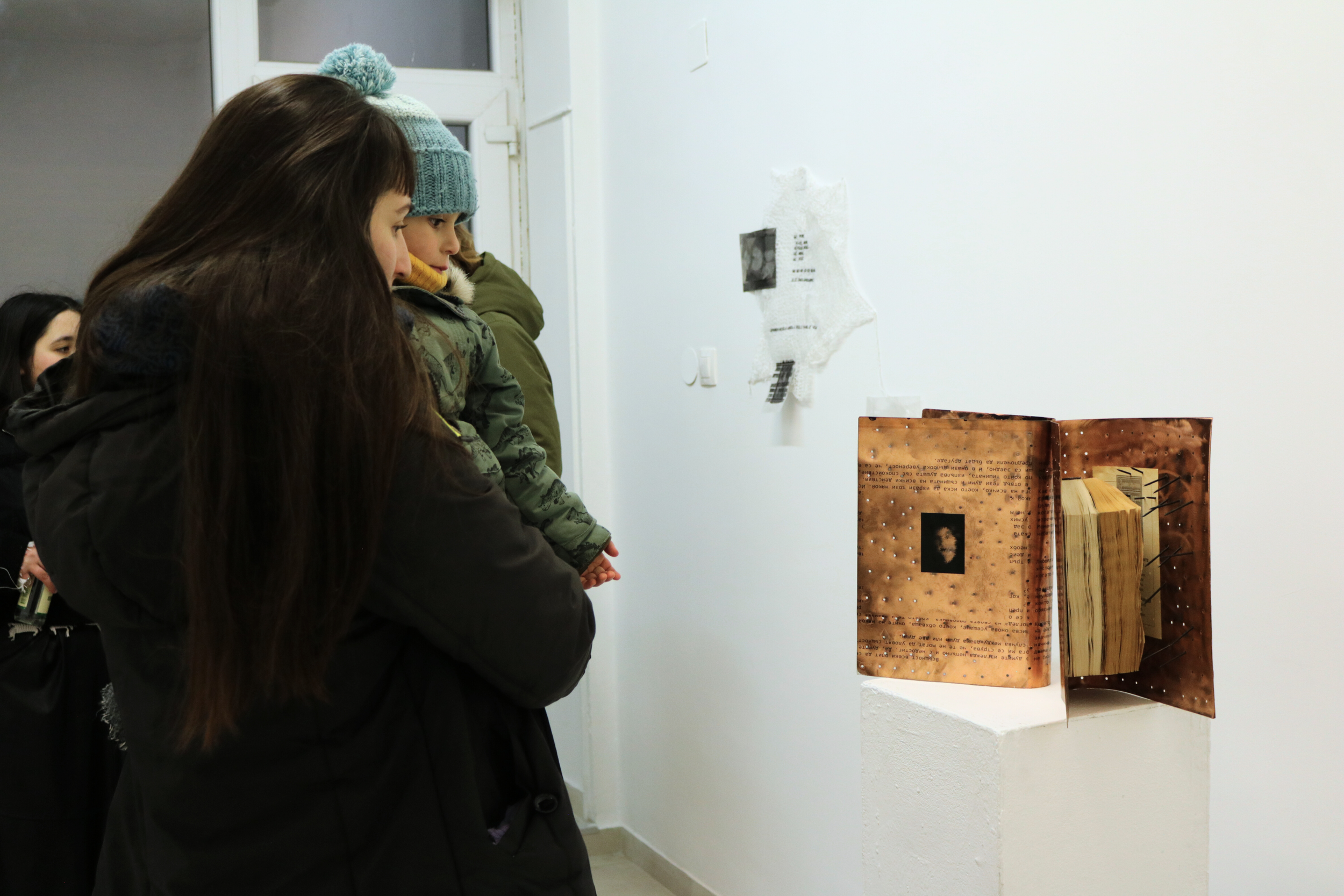 People observing an artistic book sculpture displayed in an art gallery.
