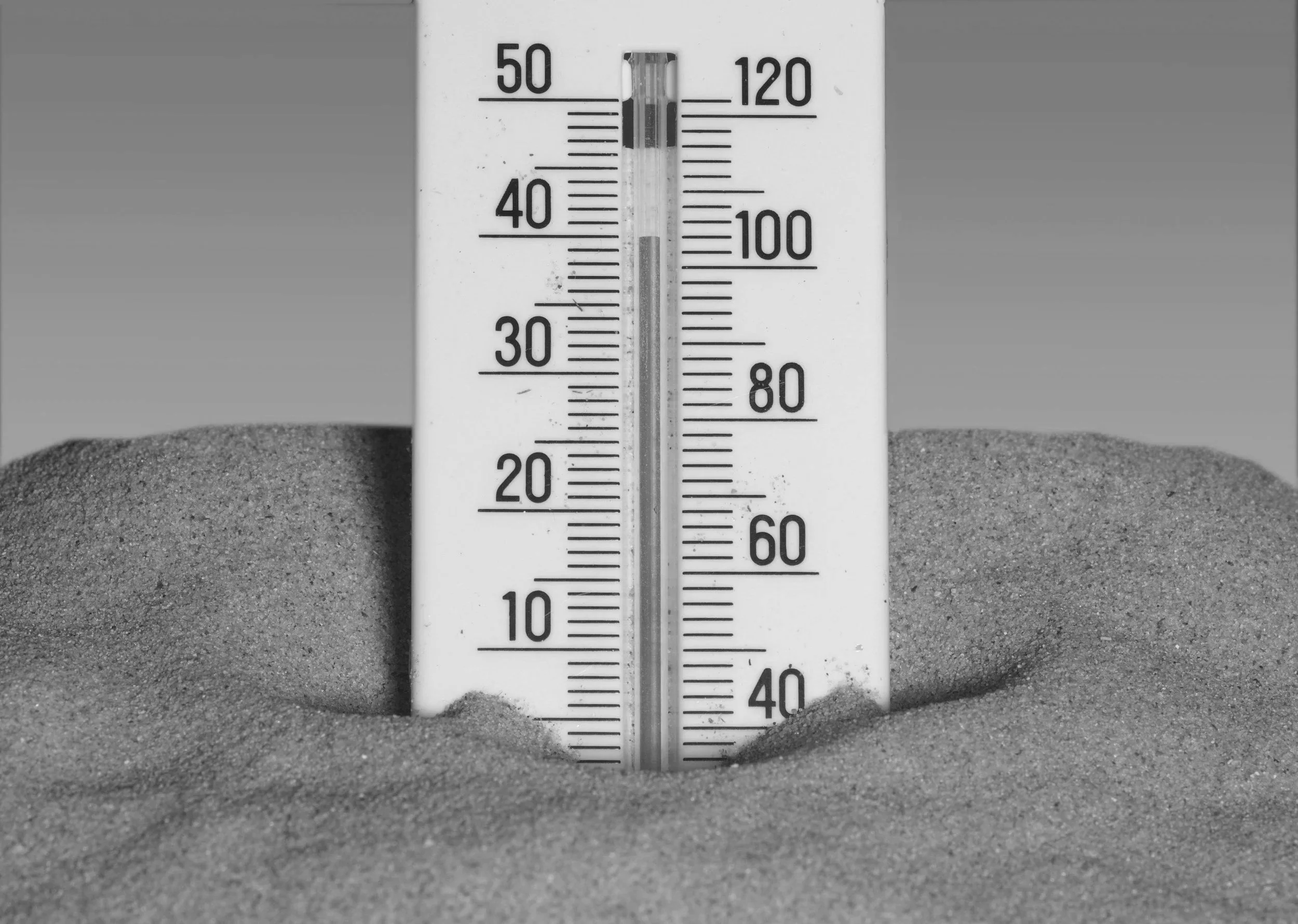 A thermometer partly submerged in sand, showing a temperature of approximately 70 degrees Fahrenheit.