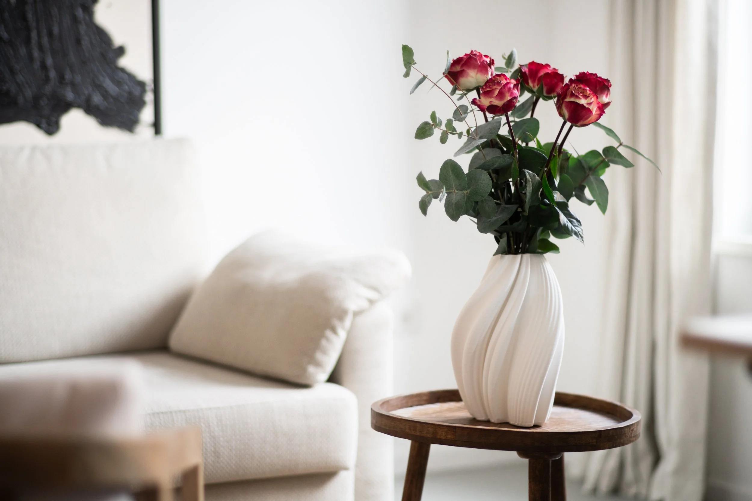 Blumenstrauß aus roten und weißen Rosen in einer weißen Vase auf einem kleinen Holztablett in der Praxis Roosen – ruhige, warme Praxisatmosphäre.