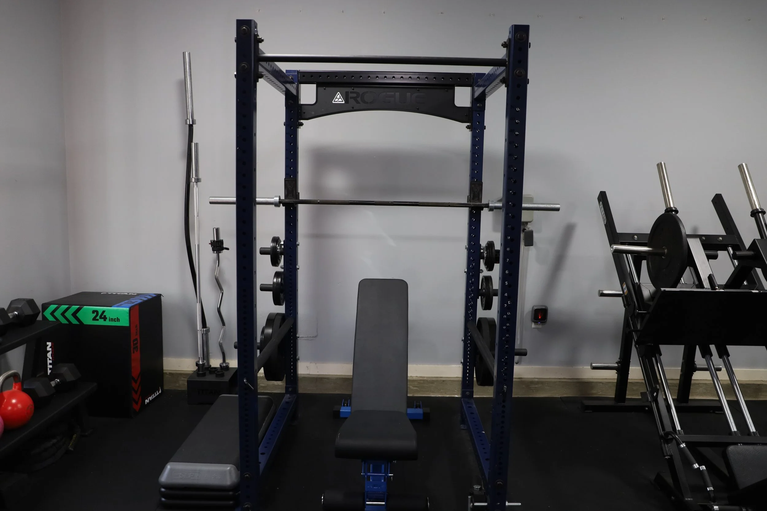 A home gym setup with a power rack, barbell, weight plates, workout bench, and other fitness equipment.