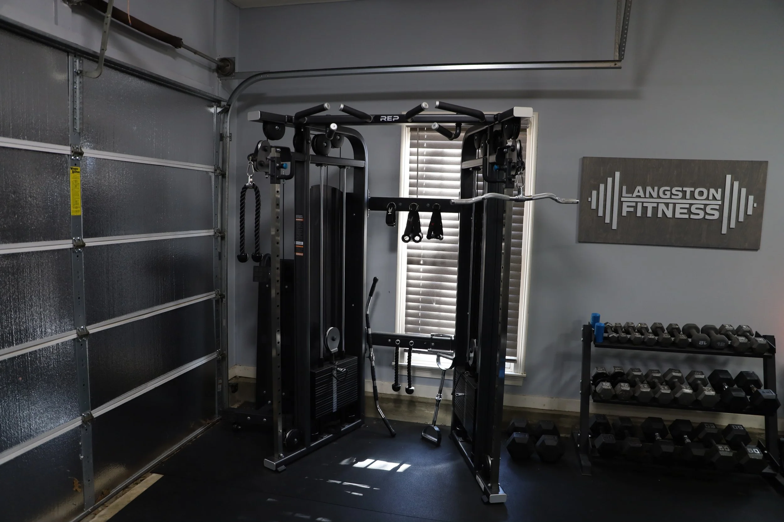 Home gym with a multifunction cable machine, free weights on a rack, and a sign that says Langston Fitness.