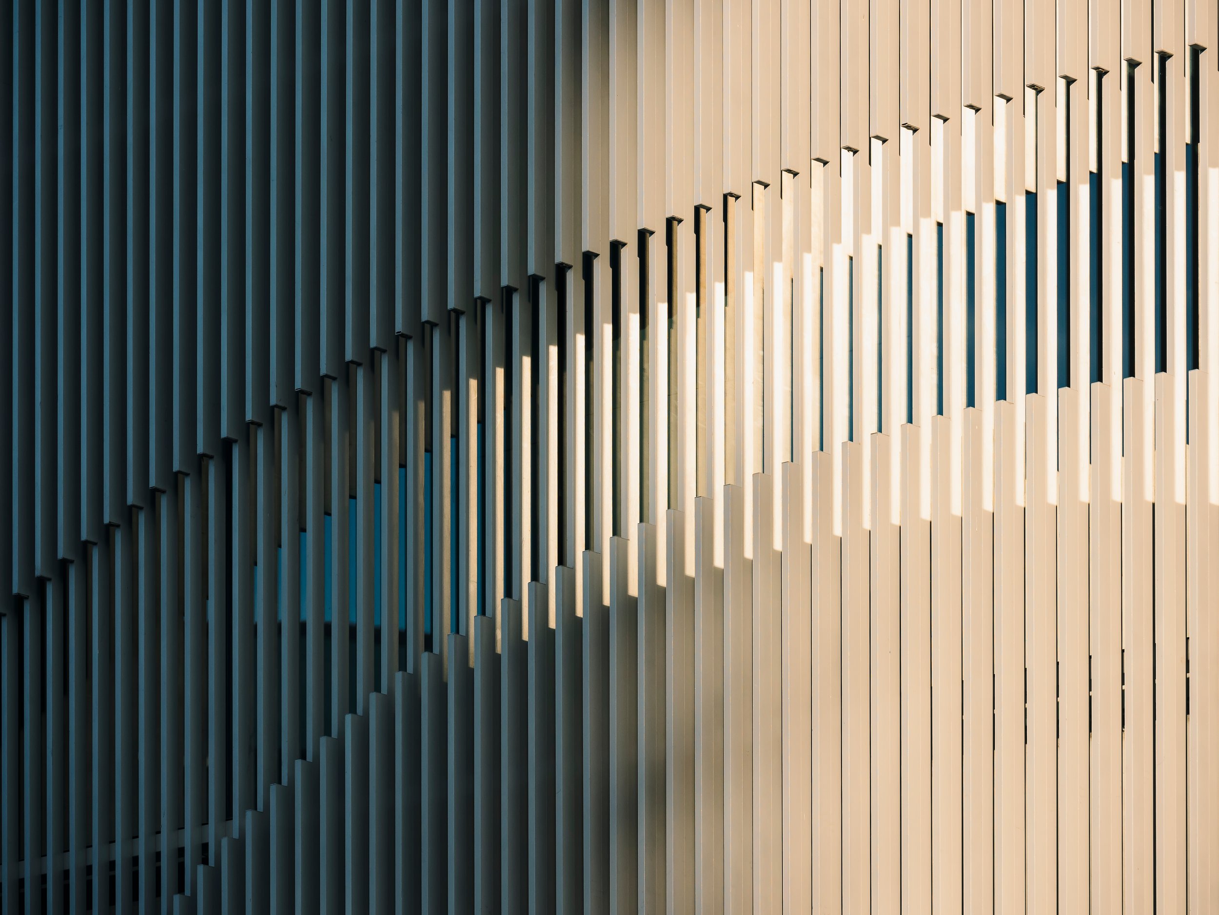 Close-up of a modern, decorative wooden wall with vertical slats arranged in a geometric pattern, illuminated by natural sunlight.